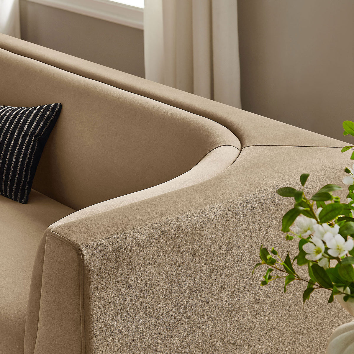 Taupe curved sofa arm styled with accent pillow and greenery, adding soft modern warmth to the living space || EEI-7564-TAU || detail_room