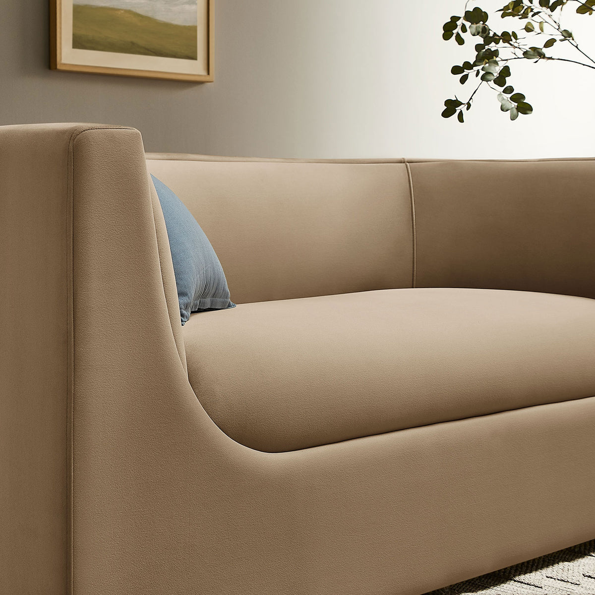 Detail of taupe velvet loveseat arm with blue accent pillow and greenery in a neutral room || EEI-7565-TAU || detail_room