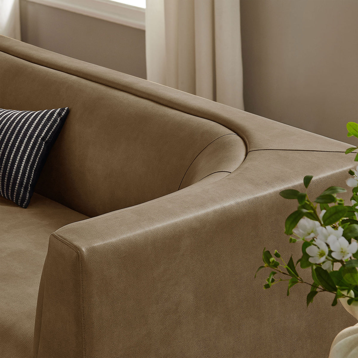 Curved back sofa corner styled with a striped accent pillow and fresh greenery in a bright living room || EEI-7567-MUS || detail_room
