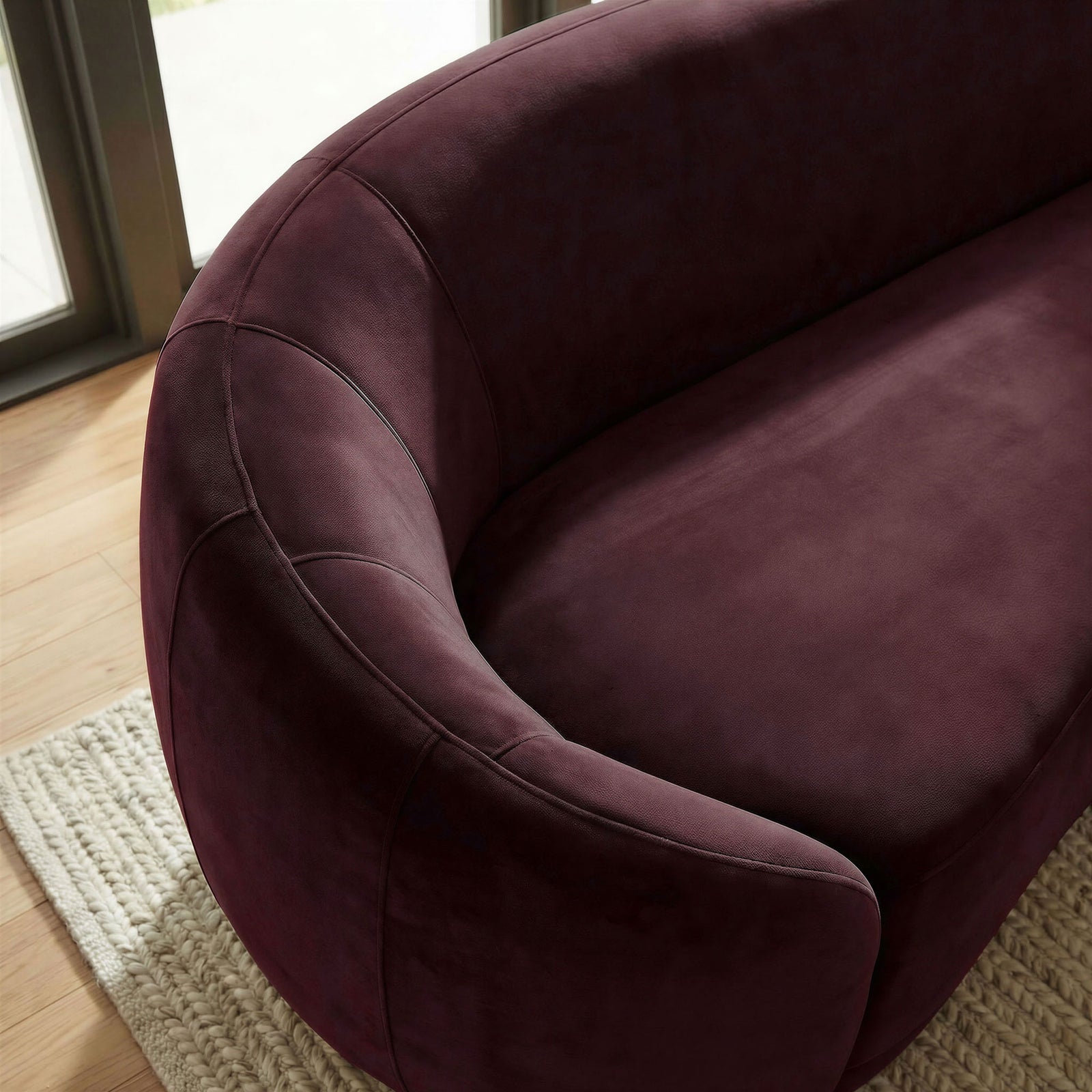 Mulberry velvet armrest catching natural light, showing the sofa's smooth texture above a woven rug. || EEI-7581-MUL || detail_room