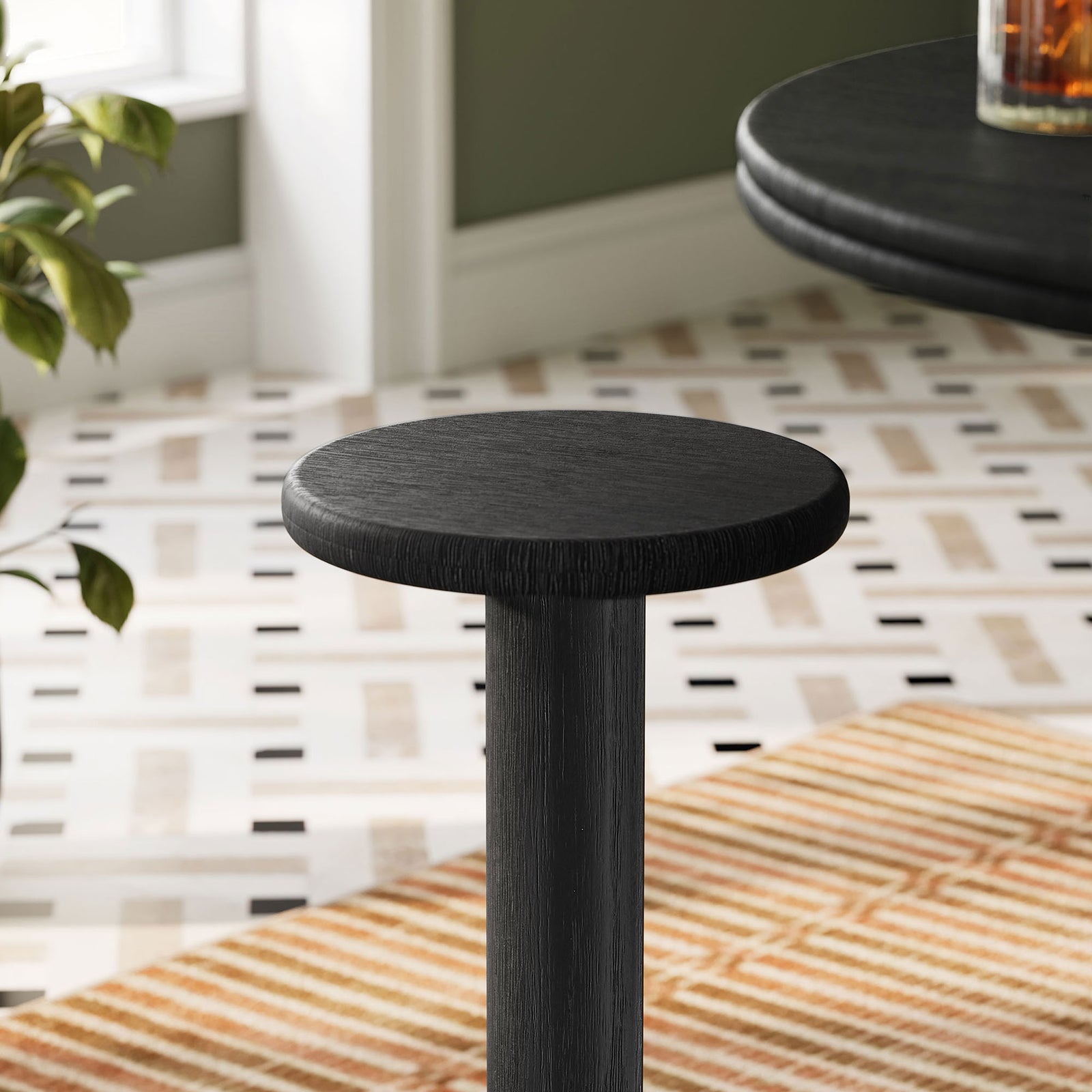 Black acacia bar stool seat styled next to a bar table in a patterned indoor dining space || EEI-7586-BLK || detail_room