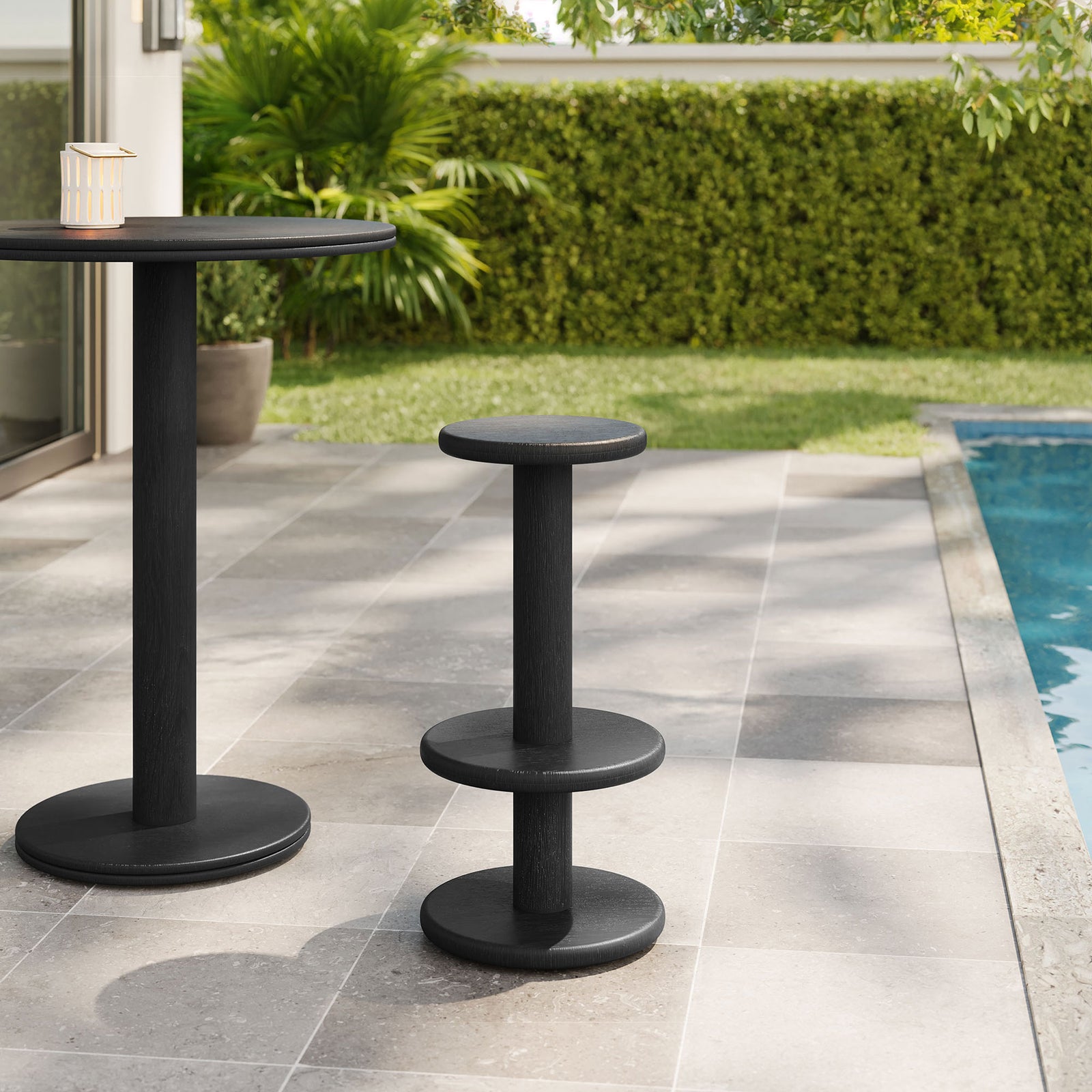 Black acacia bar stool and pedestal bar table on a poolside patio with lush greenery || EEI-7586-BLK || front_angle_room