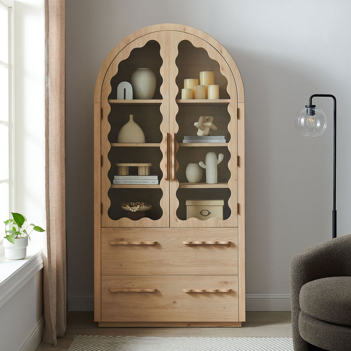 Light oak arched cabinet with scalloped glass doors and lower drawers in a cozy living space || EEI-7589-LOA || front_room
