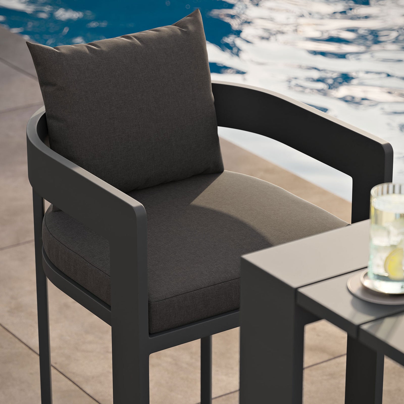 Tahoe bar chair beside a pool, highlighting the supportive charcoal cushions and dark aluminum frame. || EEI-7595-CHA || detail_room