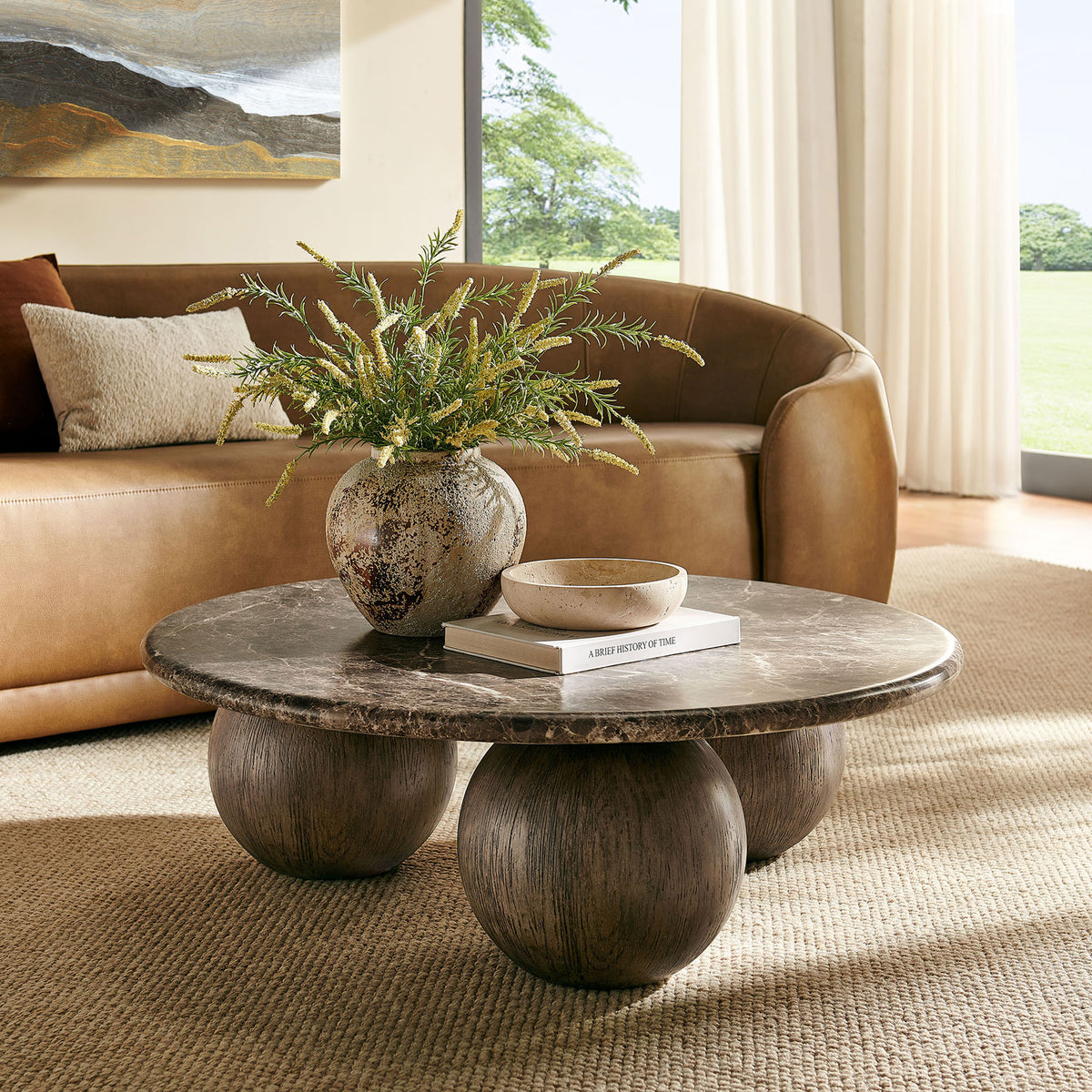 Dark marble-look round coffee table centered in a cozy living room with a curved leather sofa || EEI-7622-EMP || front_angle_room