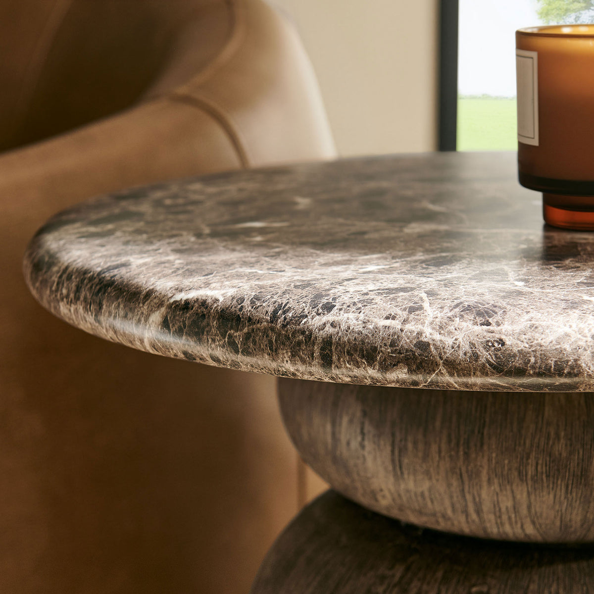 Marble-look tabletop styled with a candle beside a sofa, bringing warm texture to a cozy living space. || EEI-7625-EMP || detail_room