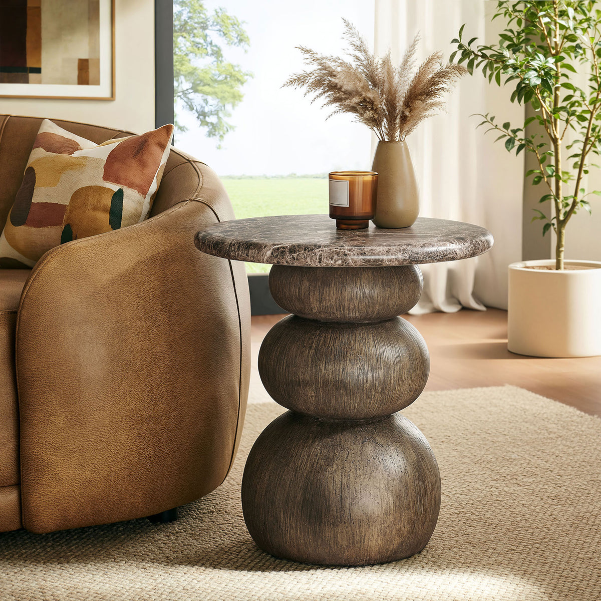 Pietra round side table beside a leather sofa, topped with decor that highlights its rich marble-look surface. || EEI-7625-EMP || front_angle_room
