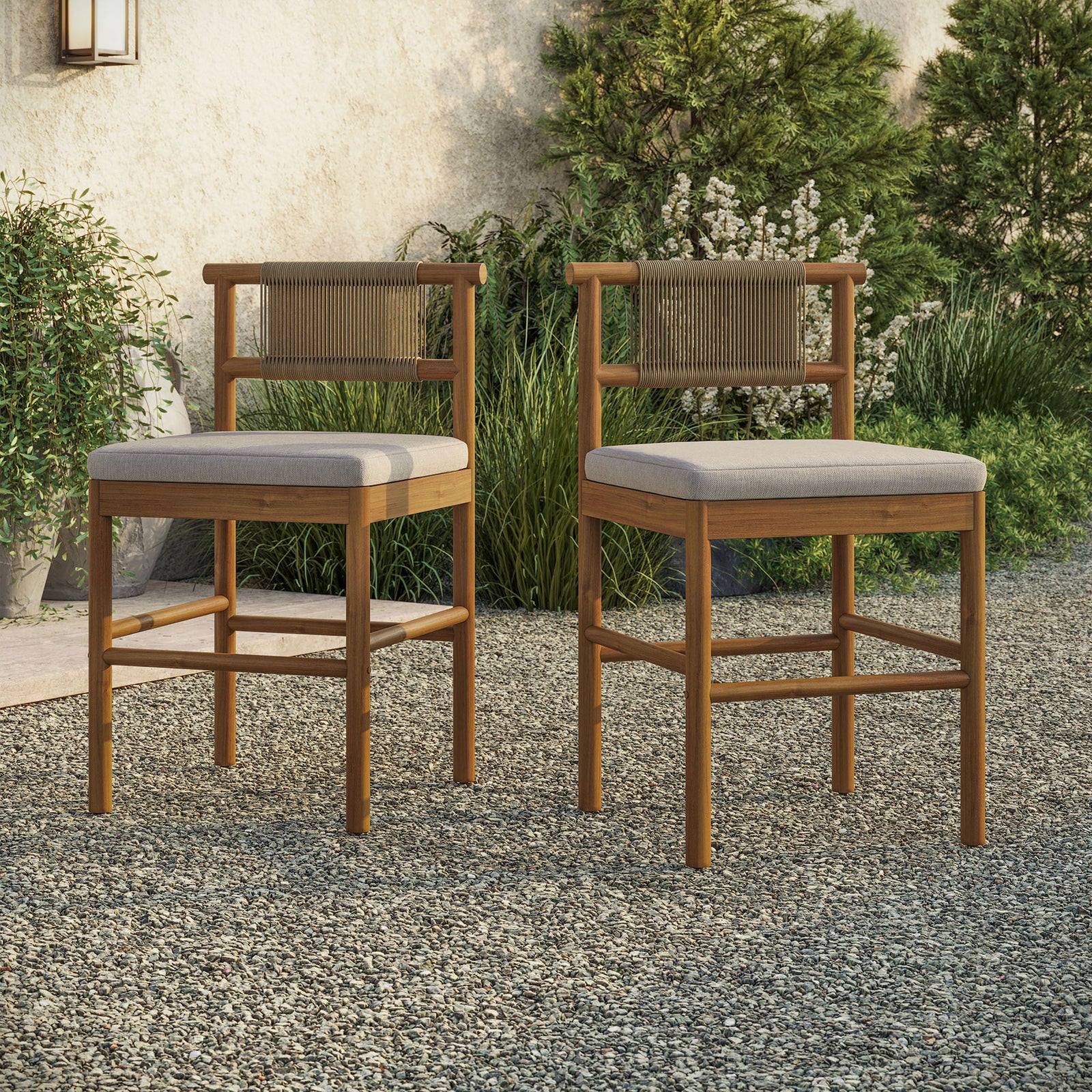 Pair of teak counter stools arranged at an outdoor bar table on a gravel patio || EEI-7627-NAT-SAI || front_angle_multi_room
