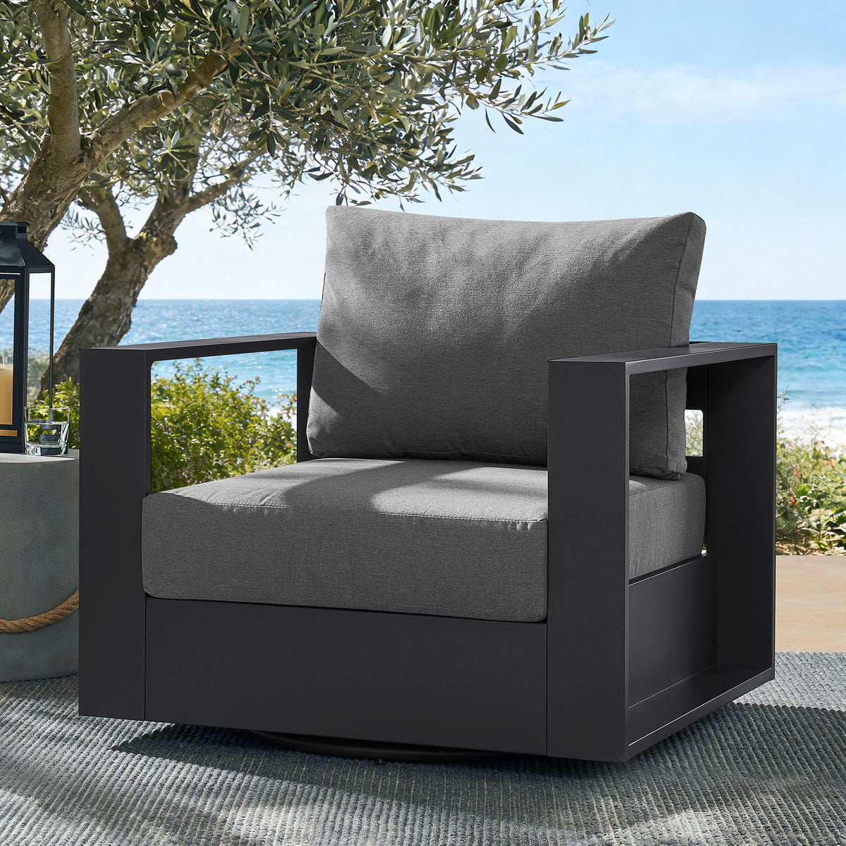 Tahoe charcoal swivel armchair styled on breezy coastal patio with outdoor rug and lantern || EEI-7728-GRY-CHA || front_angle_room