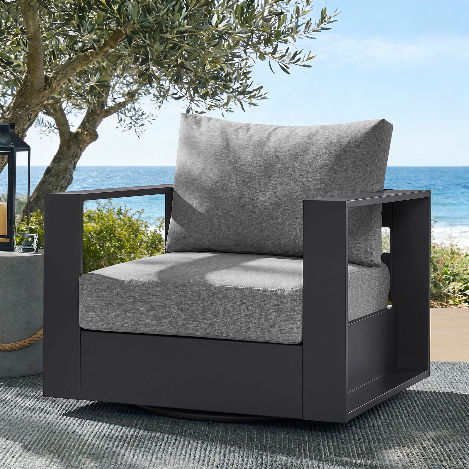 Tahoe swivel armchair with light gray cushions styled on coastal patio beside lantern and side table || EEI-7728-GRY-GRY || front_angle_room