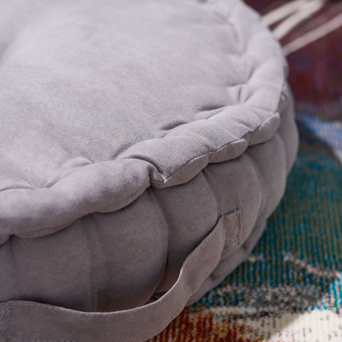 Soft gray fabric, plump trim, and a sewn-on handle bring texture to this cozy floor cushion