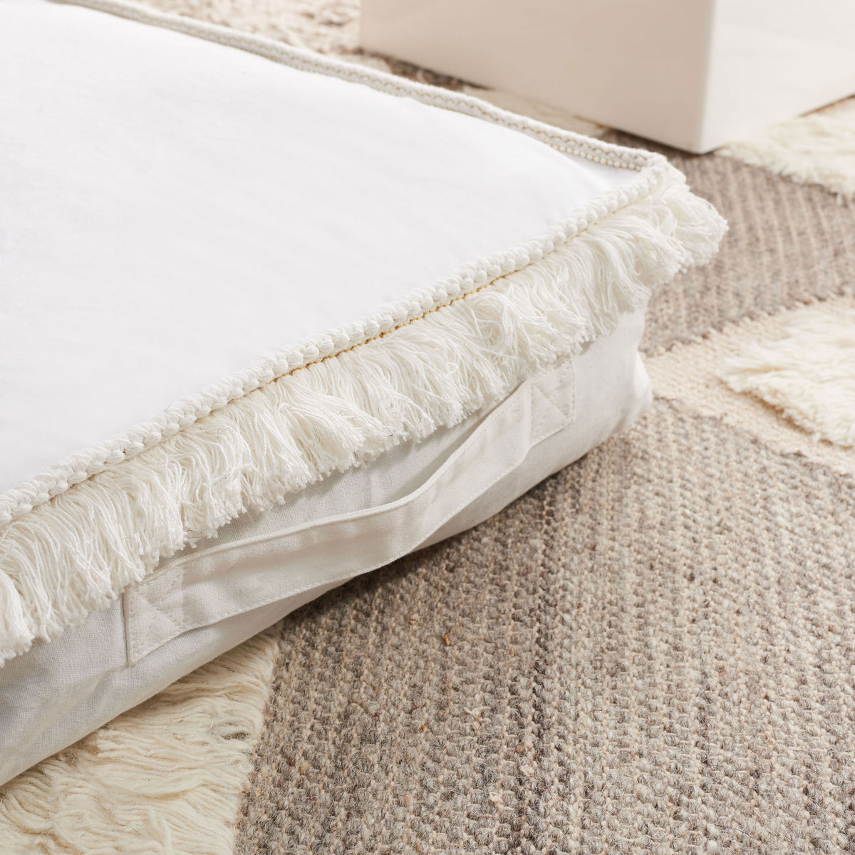 Fluffy ivory fringe and a slim fabric handle add texture and portability to this floor cushion.