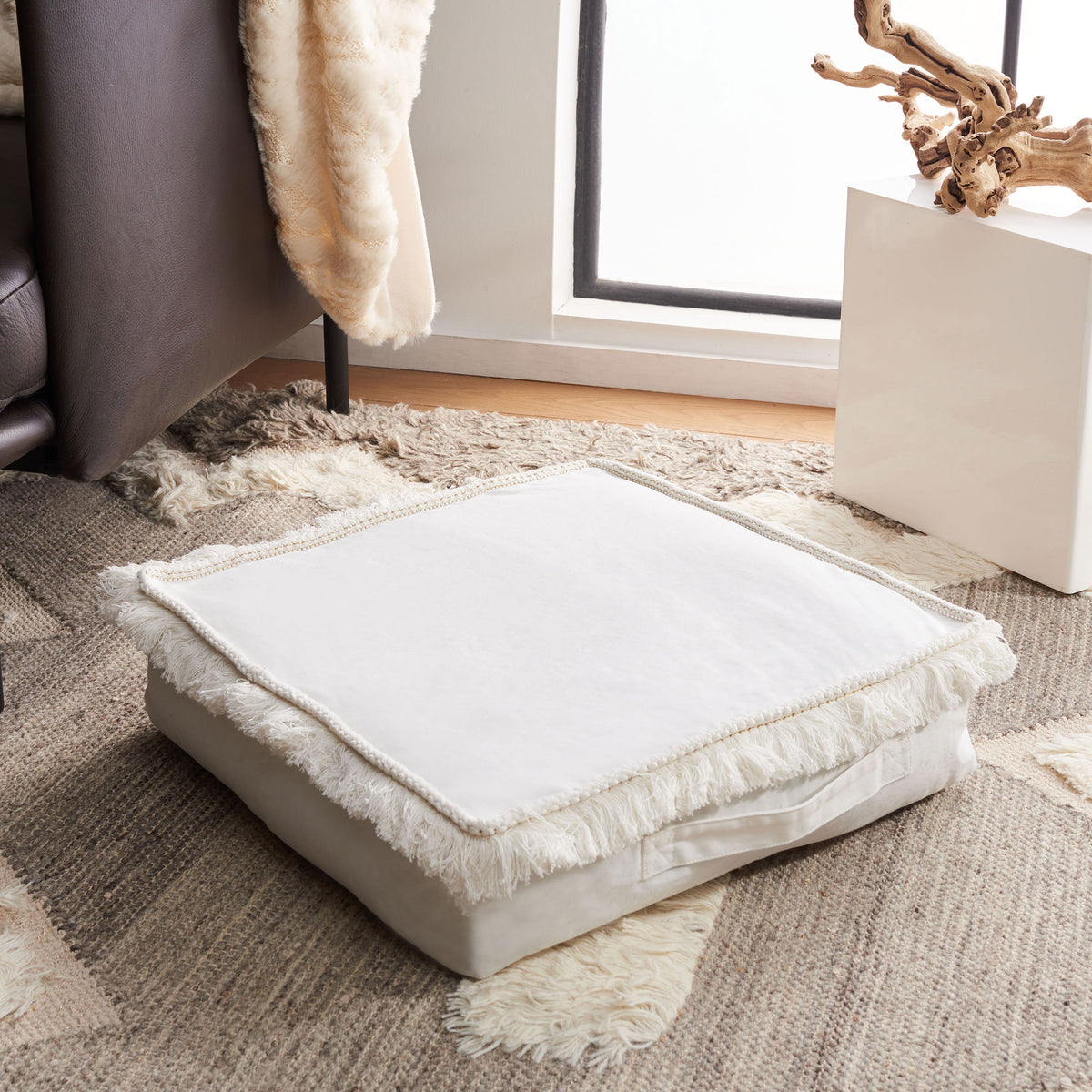 A plush ivory floor cushion with a clean center and billowy fringe offers a cozy place to unwind. || FLP1018A || front_angle_room
