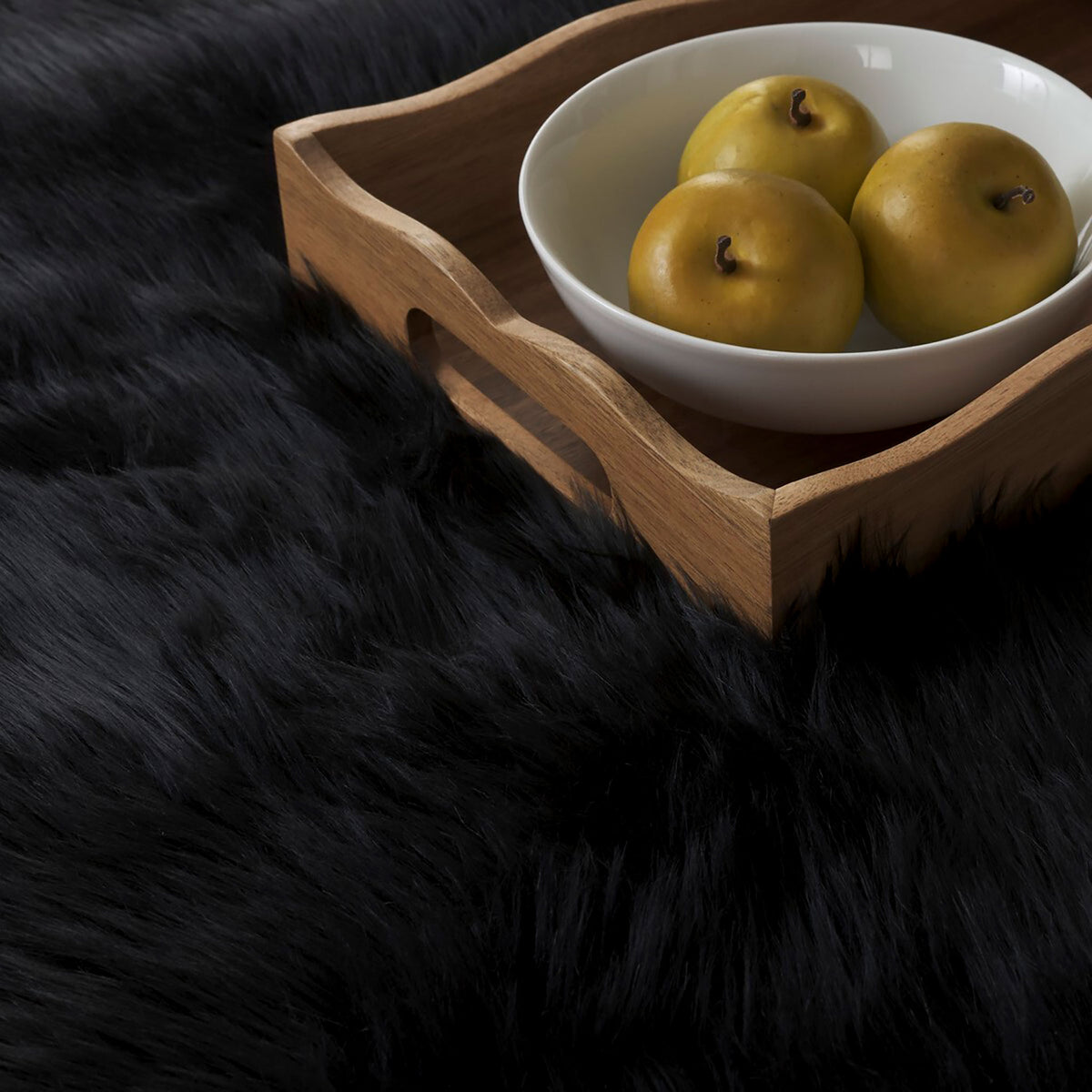 Close-up of plush black faux sheepskin fur beside a wooden tray with a bowl of apples