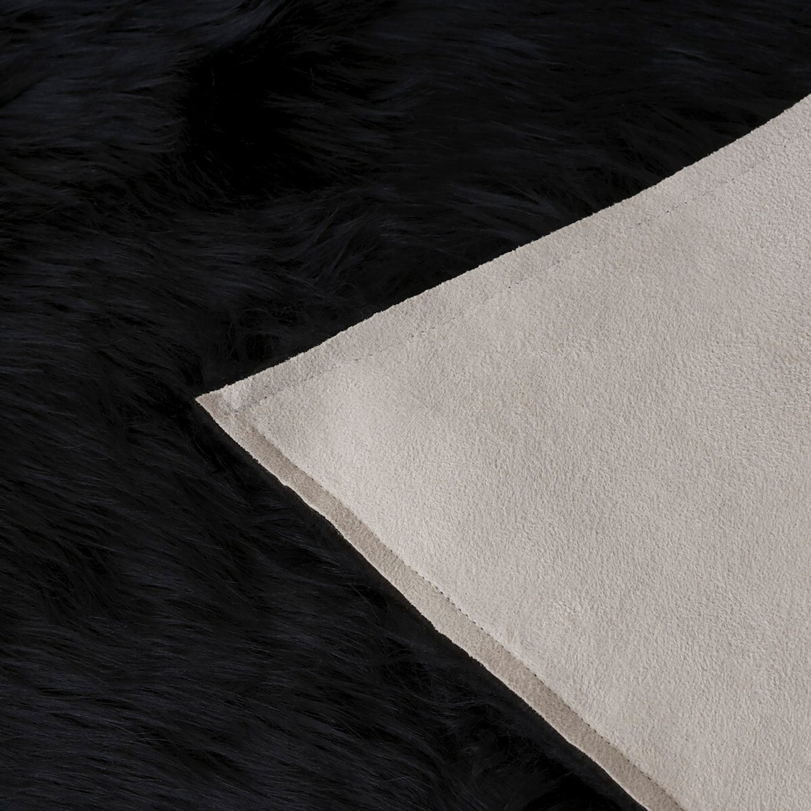 Folded black faux sheepskin rug revealing a pale fabric backing beneath the long fur || FSS115B-2 || backing_studio