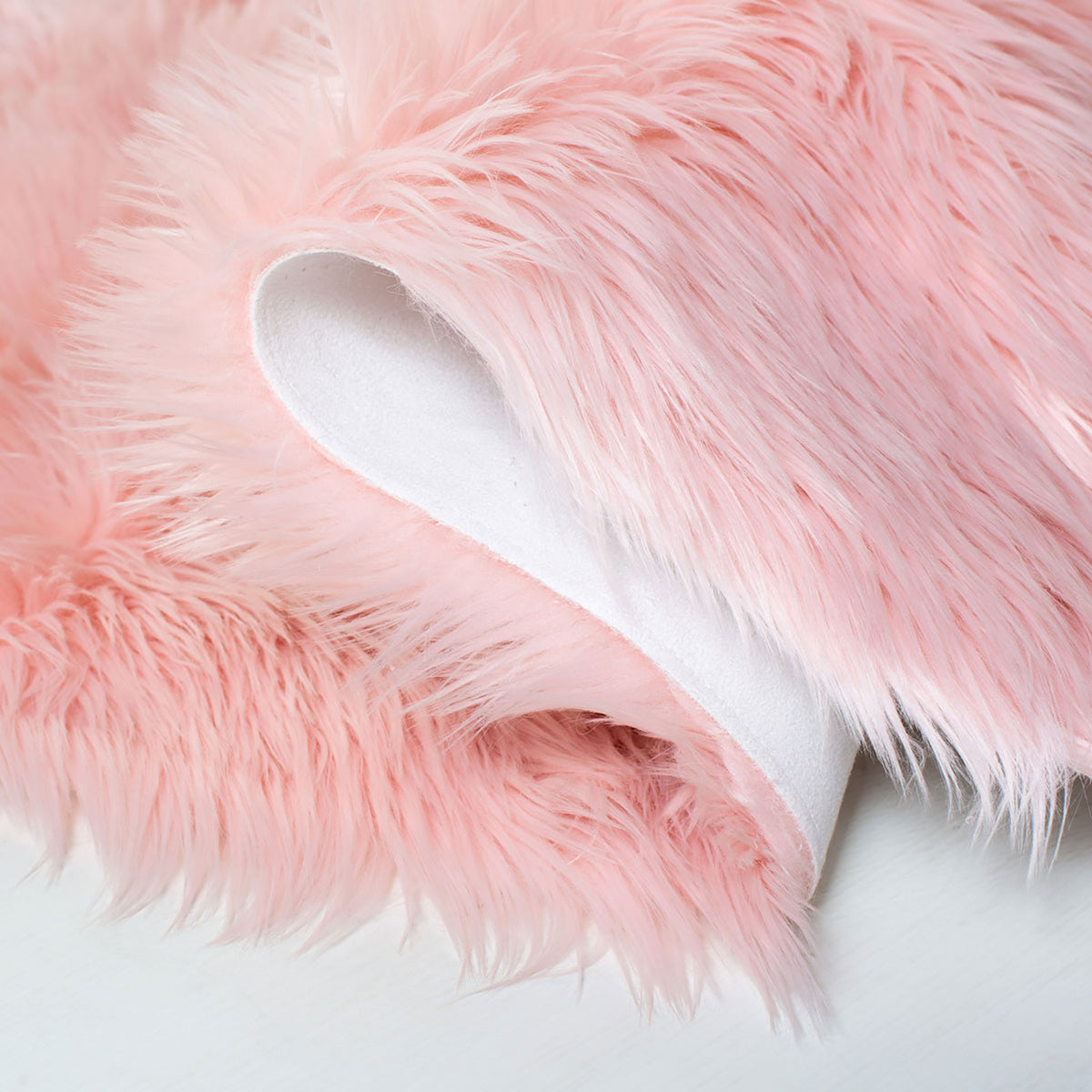 Close-up of pink faux sheepskin fur, folded to showcase white fabric backing with stitched edges || FSS235G-5 || fold_room