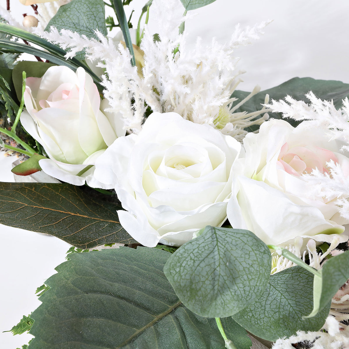 Ivory roses nestle among fern leaves and feathery white accents.