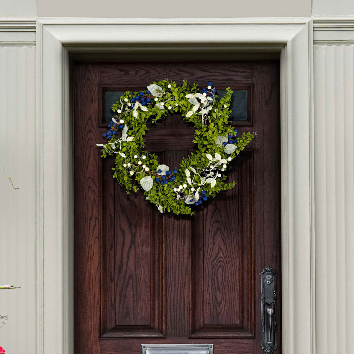 Blue and white berries brighten a green boxwood wreath on a wood door.