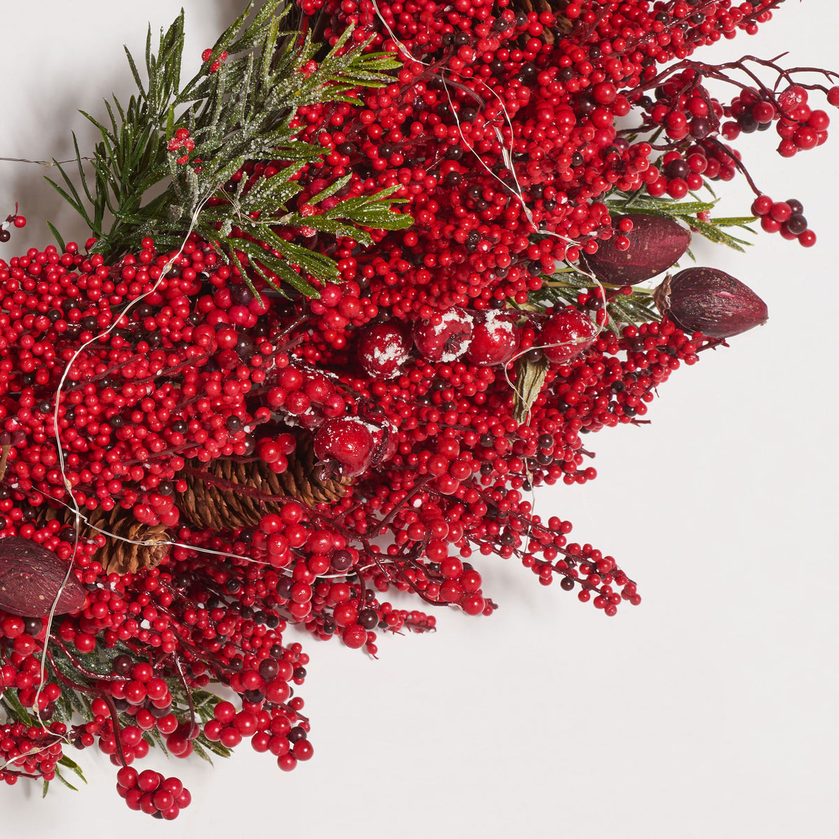 Dense red berries, pine needles, and tiny LED wires add layered texture.