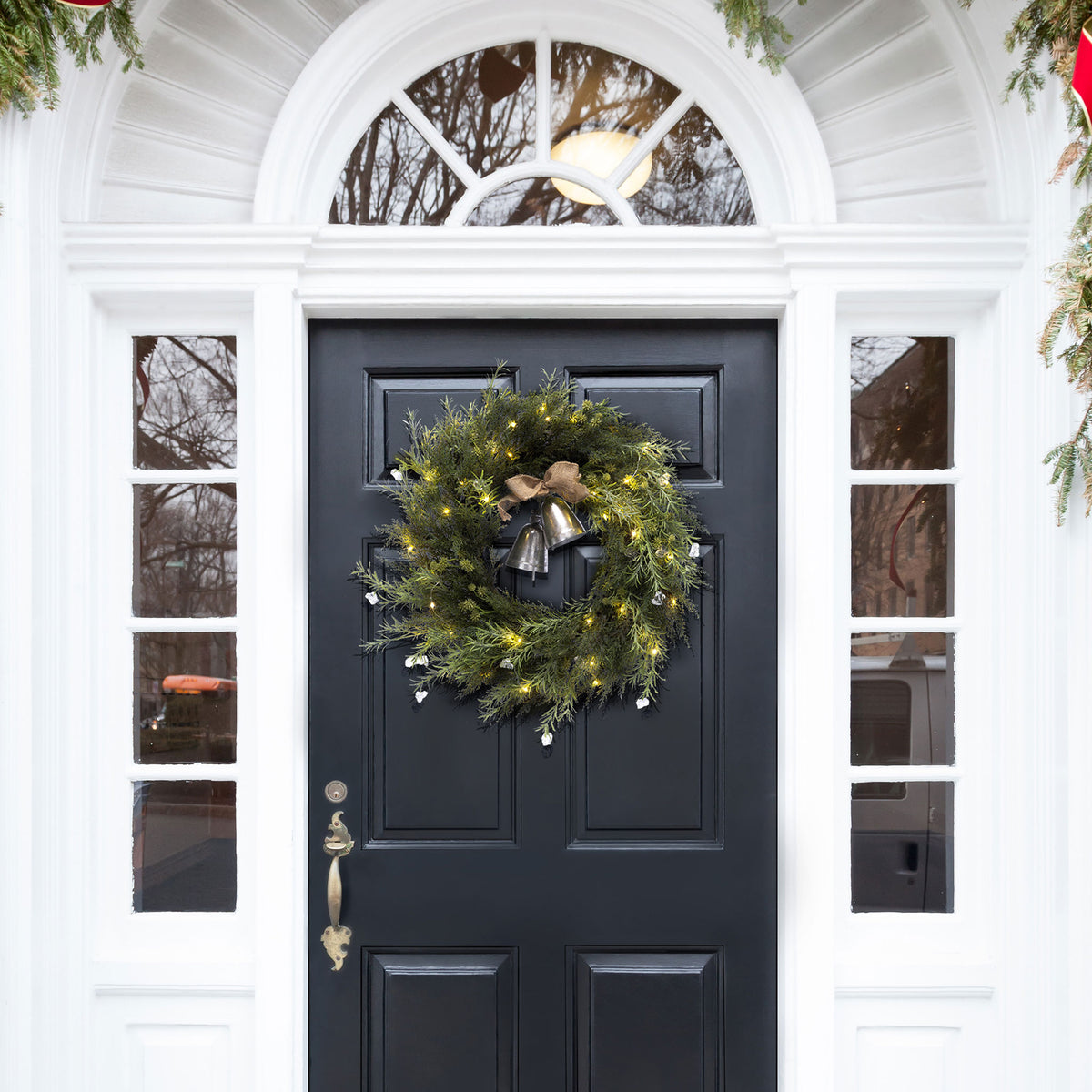 An illuminated evergreen wreath welcomes the season from a dark door.