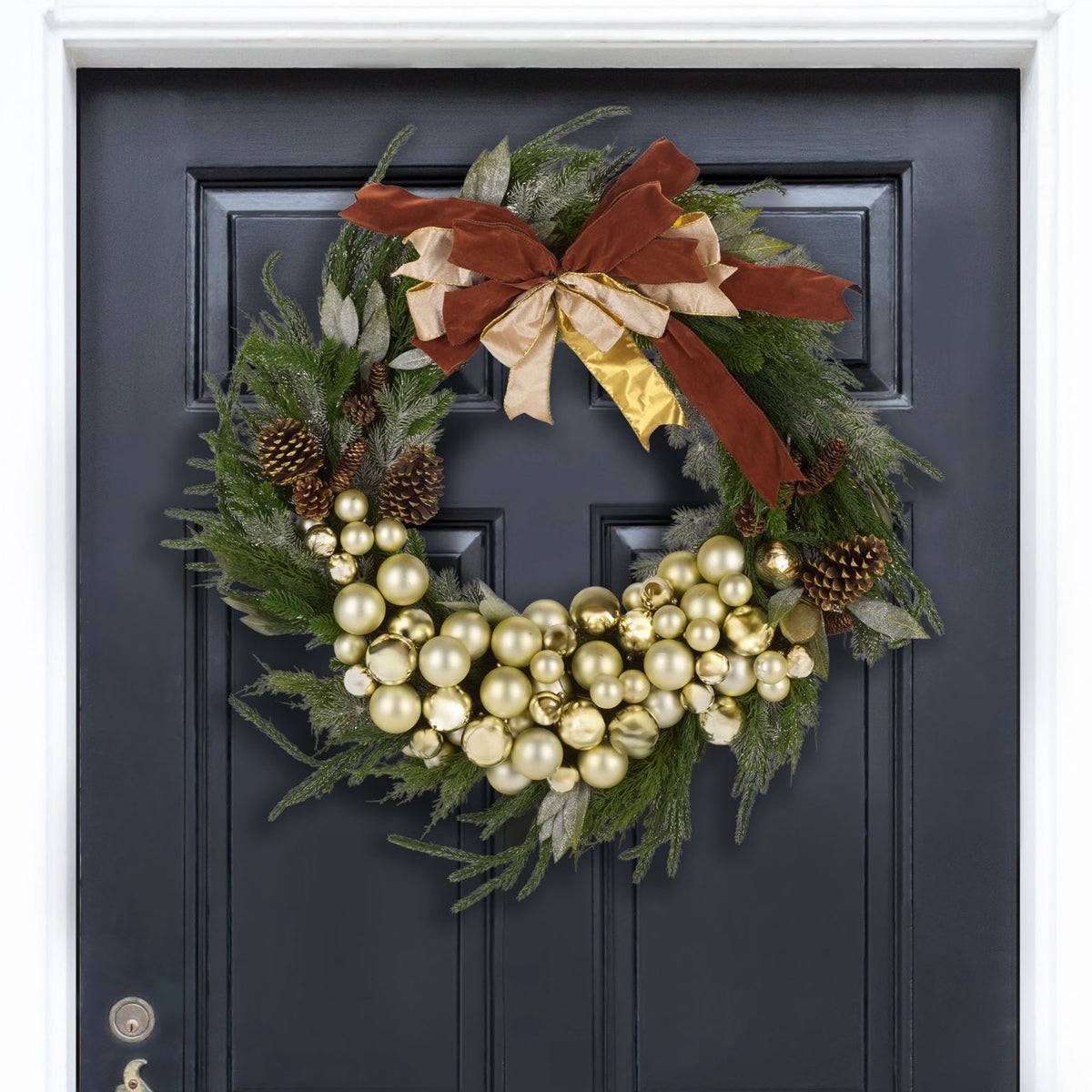 A layered rust and gold bow tops a lush wreath of pine cones and champagne ornaments.