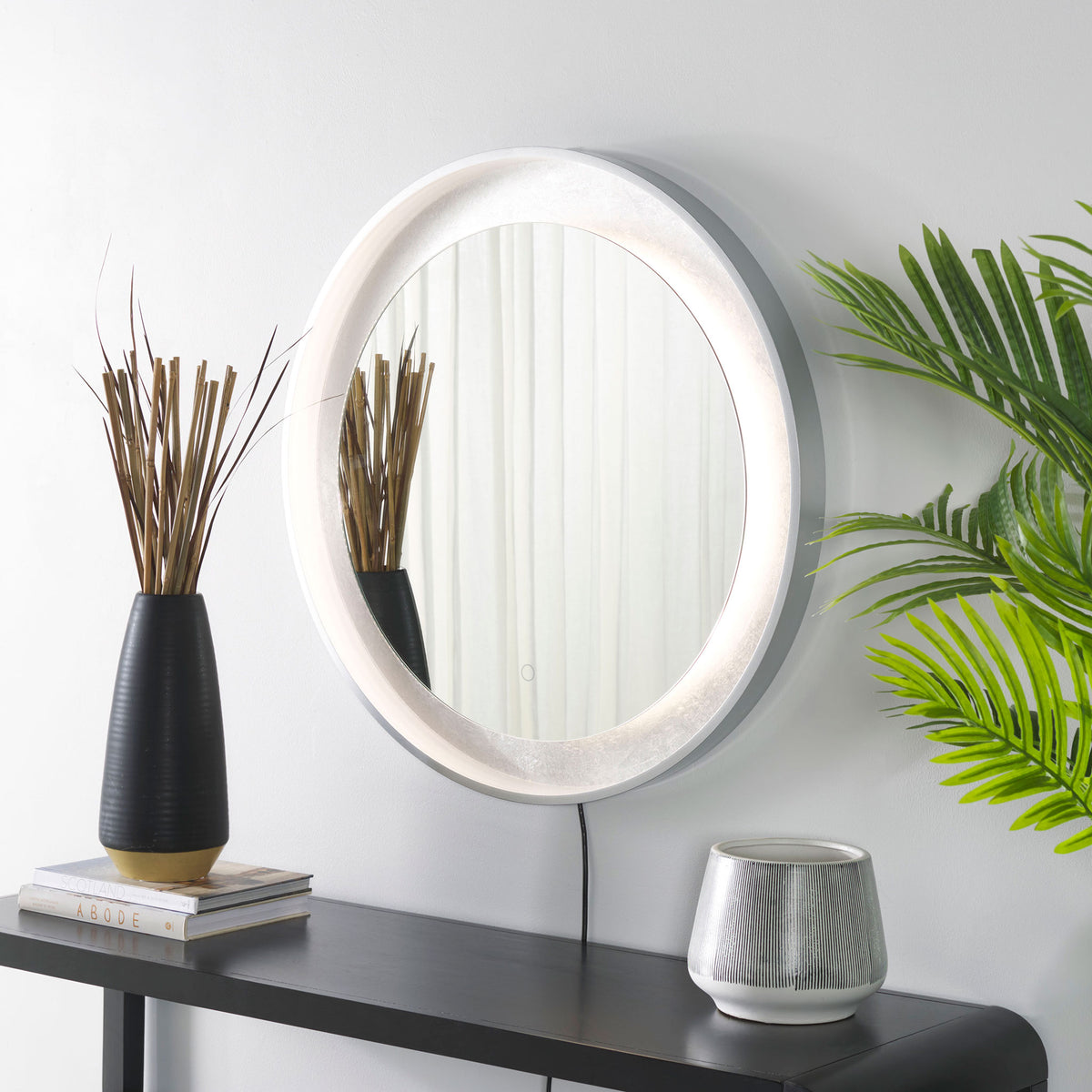 Bright LED light highlights the silver-leaf border of a silver-gray mirror above a console.