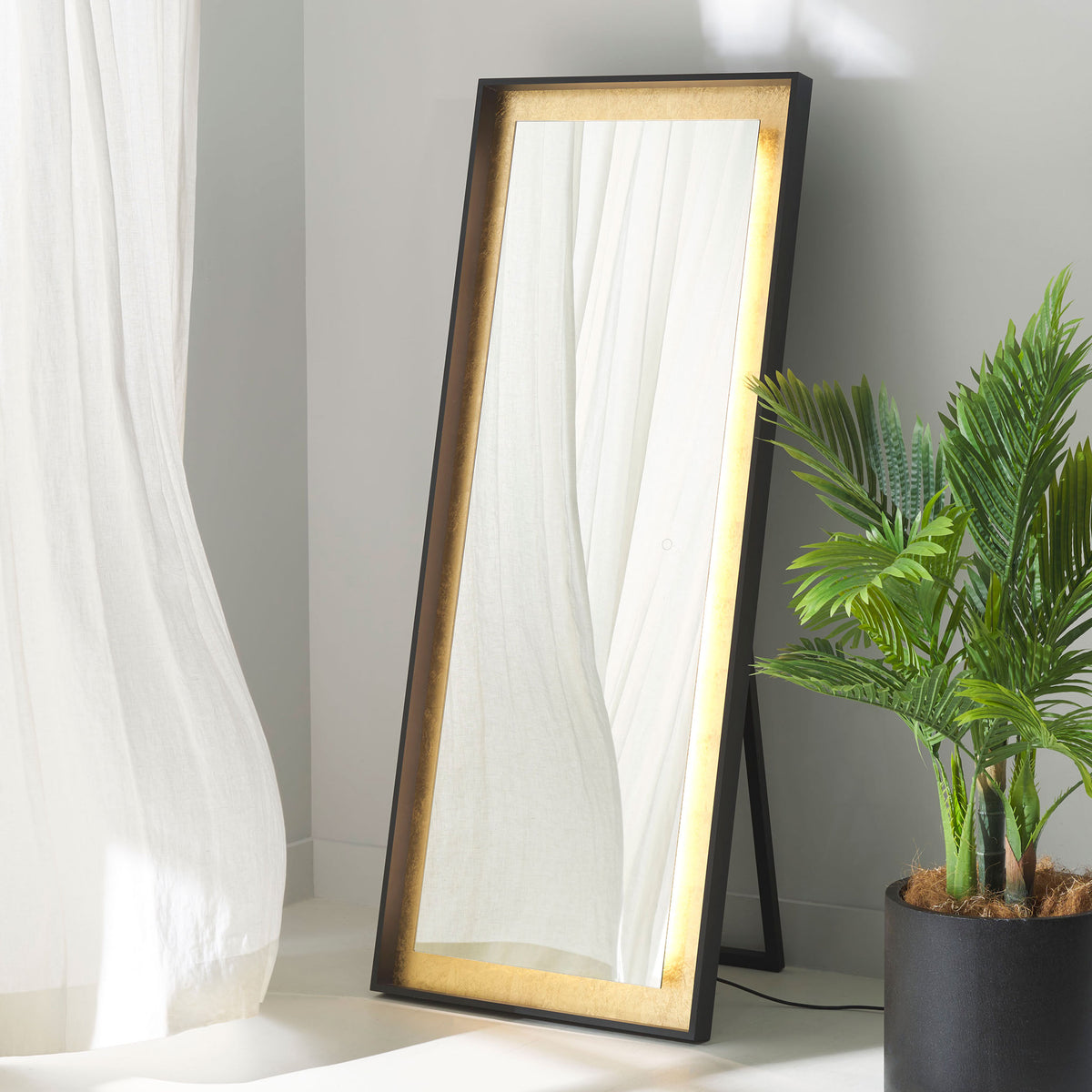 A glowing gold leaf border adds warm ambience to this black-framed freestanding mirror. || LMR1015B || front_angle_on_room