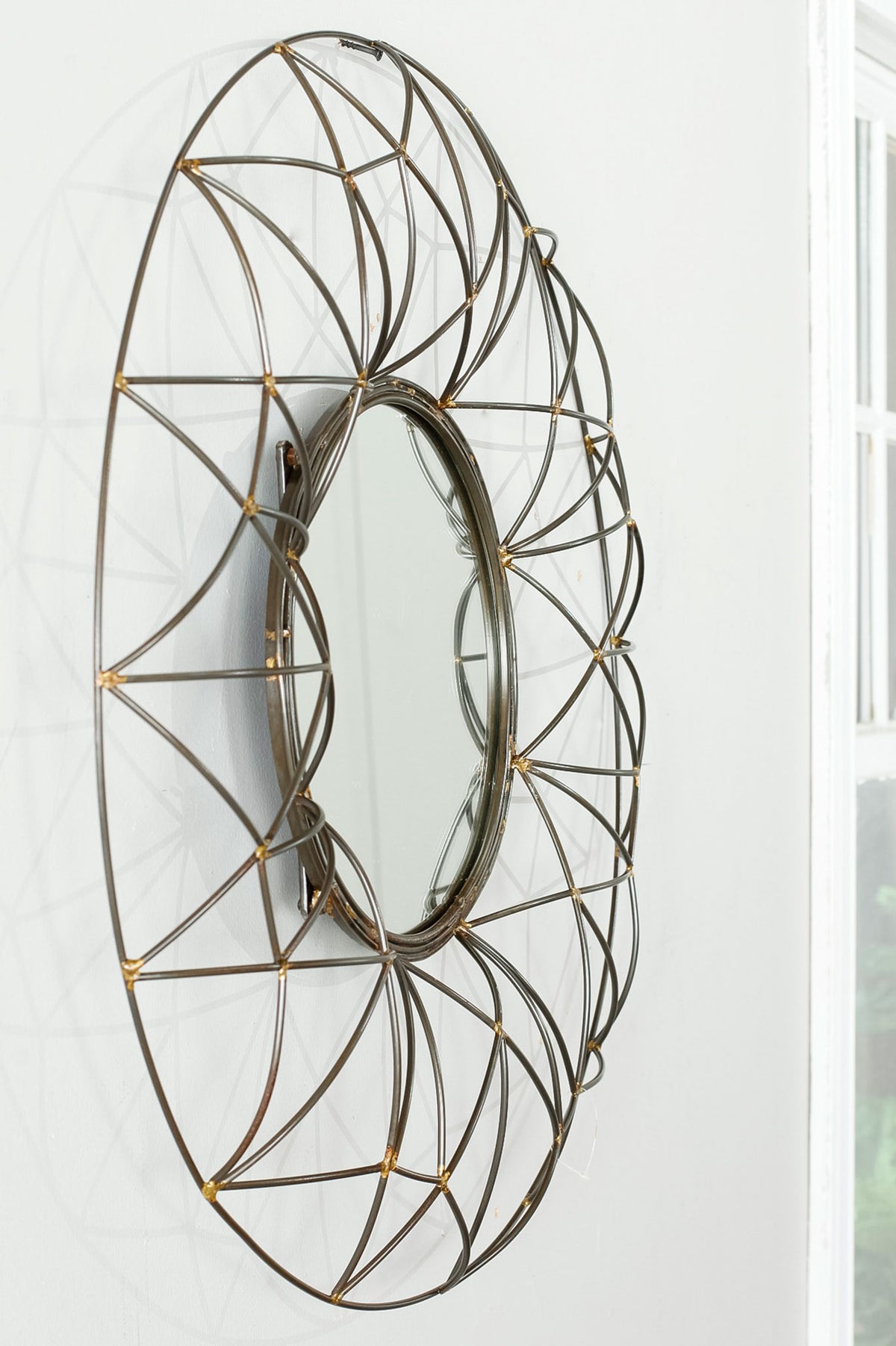 A dimensional bronze wire lattice creates an airy, sculptural frame around the round wall mirror.