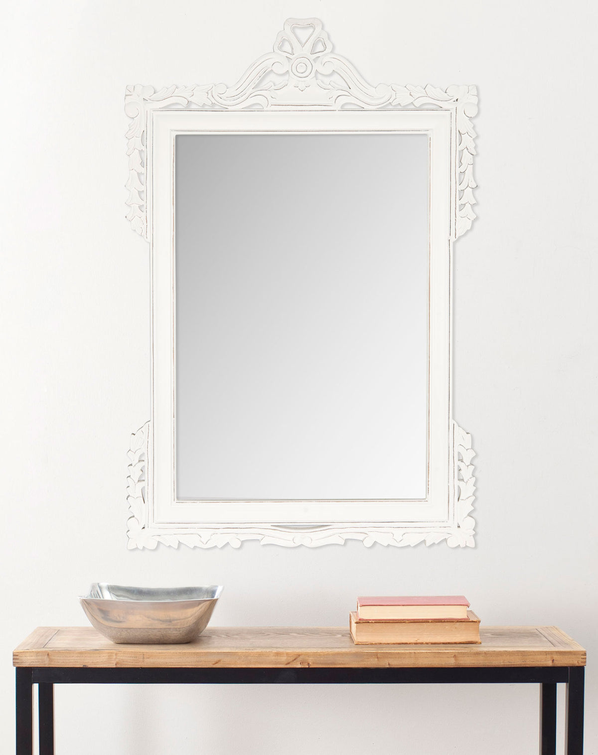 An antique white mirror with a scrolling crest brings classic elegance above a console || MIR5004D || front_room