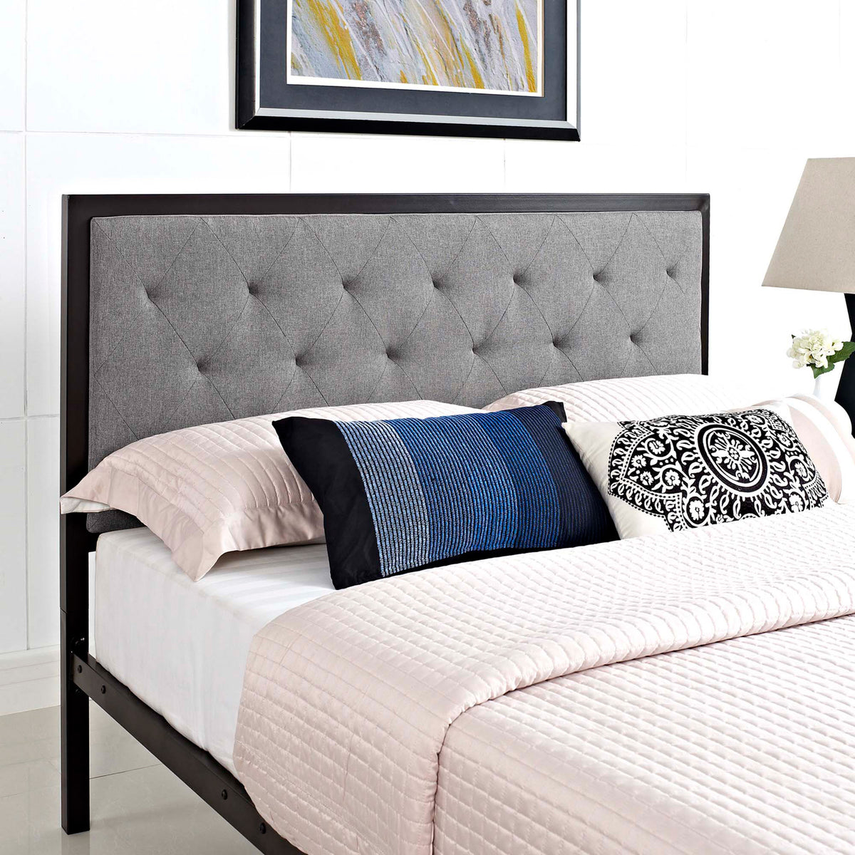 A plush gray headboard adds diamond tufting and a tailored border behind layered pillows.