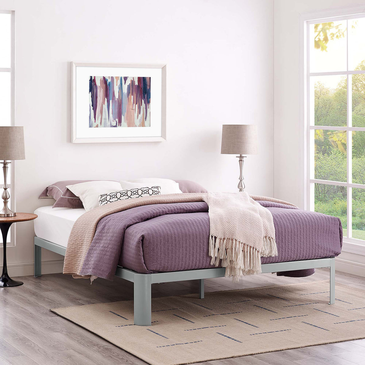 A gray platform bed frame complements purple bedding in a bright bedroom.