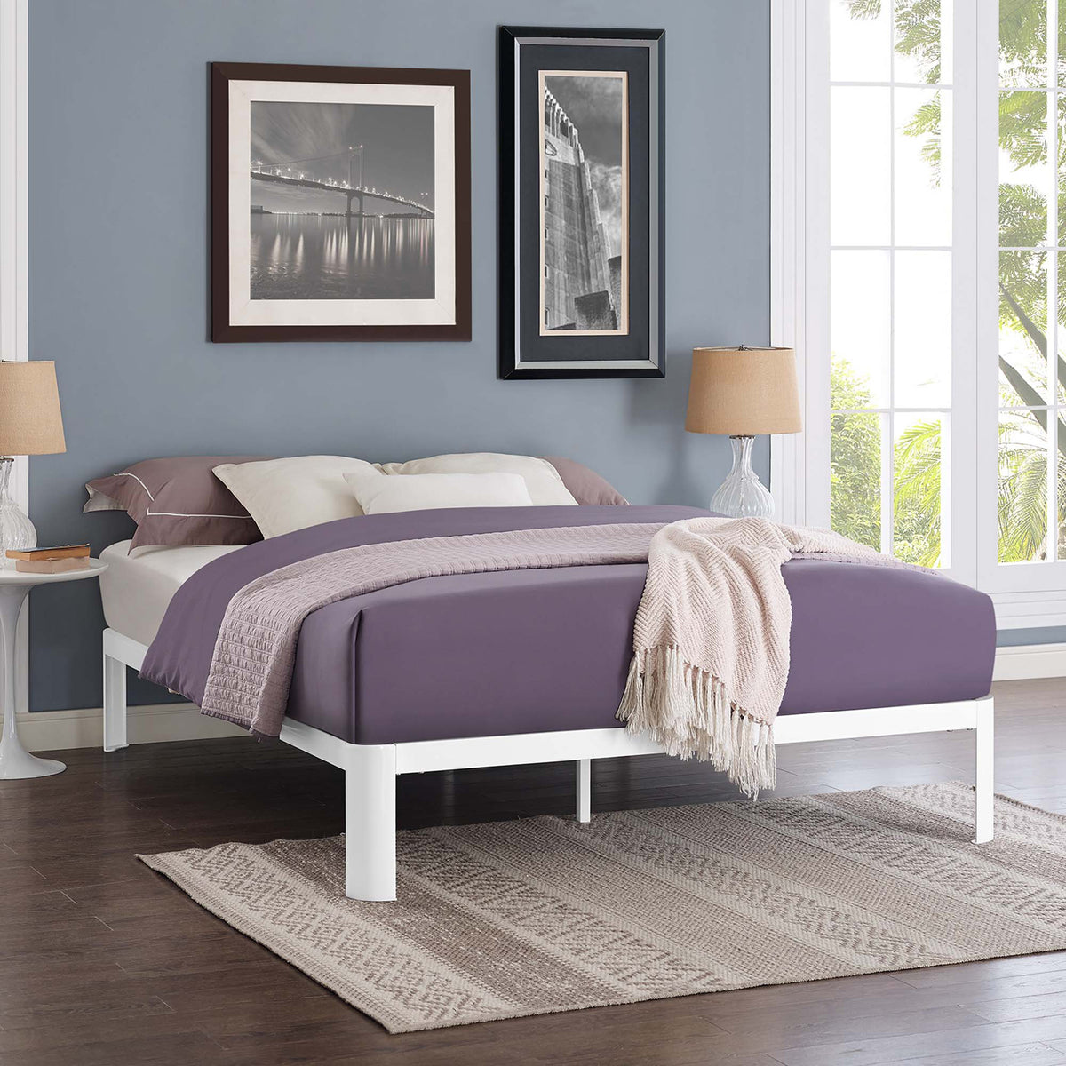 A white platform bed frame adds a crisp foundation beneath rich purple bedding.