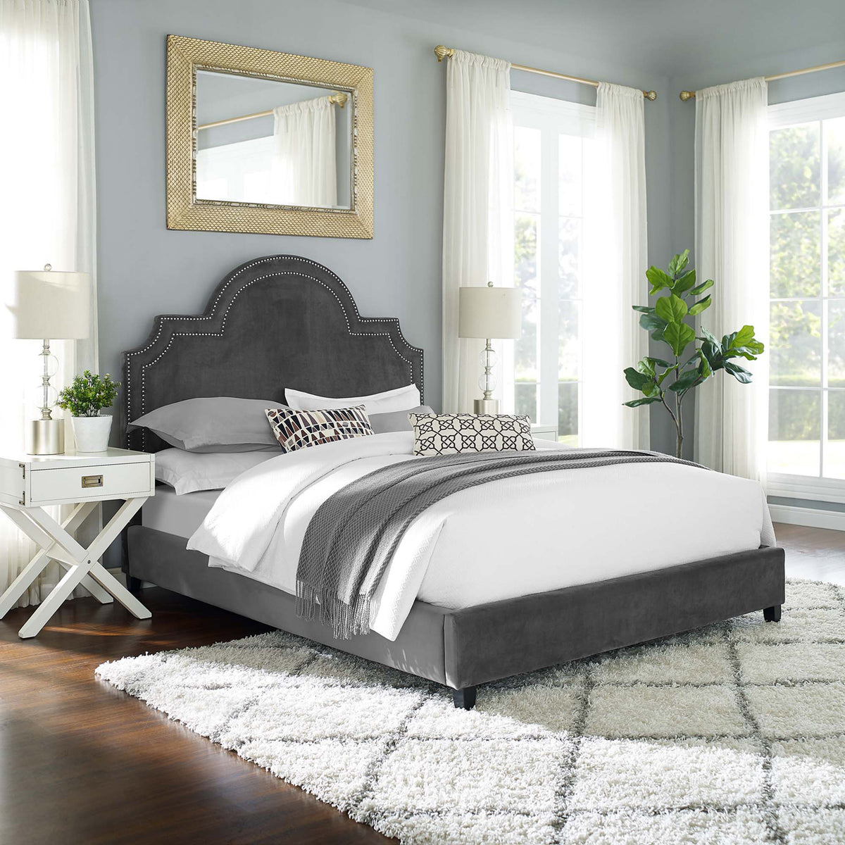 An arched headboard with nailhead trim and a gray velvet frame bring classic elegance to the bedroom