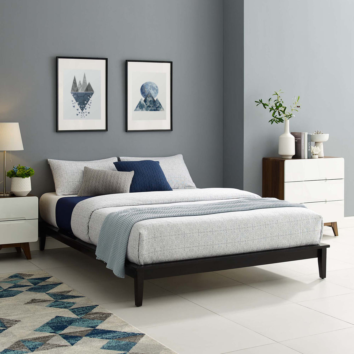 Dark wood platform bed with slim rails and tapered legs complements layered blue and white bedding