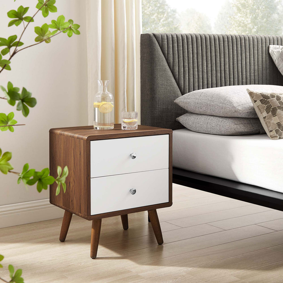 Mid-century nightstand in a bright bedroom, pairing walnut wood and white drawers beside a modern upholstered bed. || MOD-7017-WAL-WHI || front_angle_room