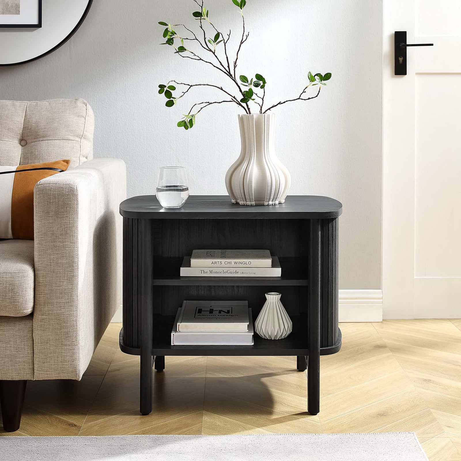 Modern black nightstand used as a side table beside a sofa, topped with a vase and glass with books below || MOD-7157-BLK || front_angle_room