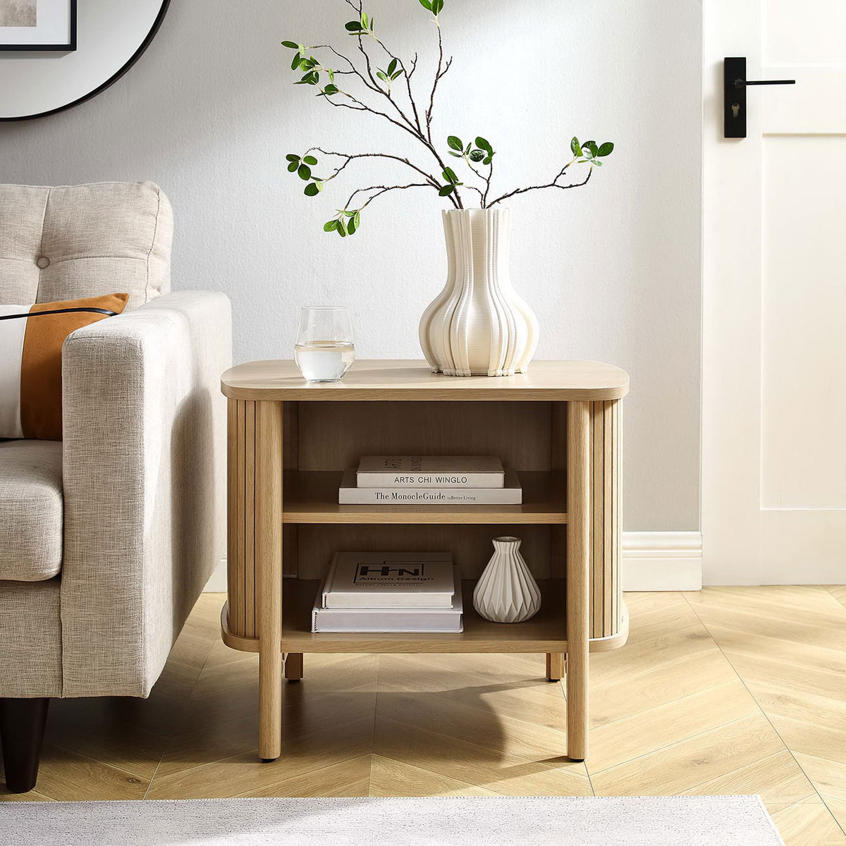 Cadence oak nightstand used as a living room side table, displaying decor and books on its open, airy shelving || MOD-7157-OAK || front_angle_room