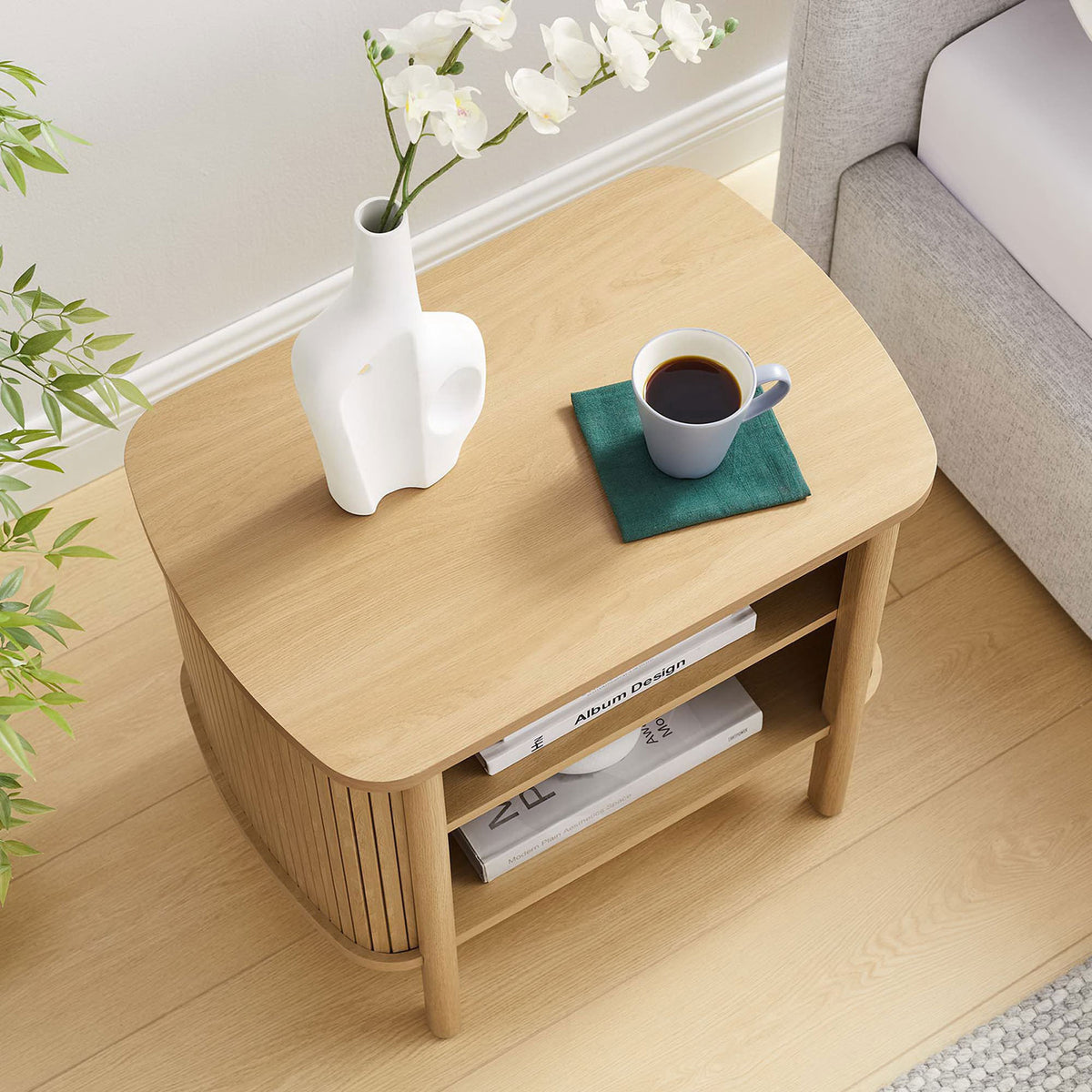 Styled Cadence oak nightstand with books, vase, and coffee, showcasing generous tabletop and open storage in use || MOD-7157-OAK || top_angle_room