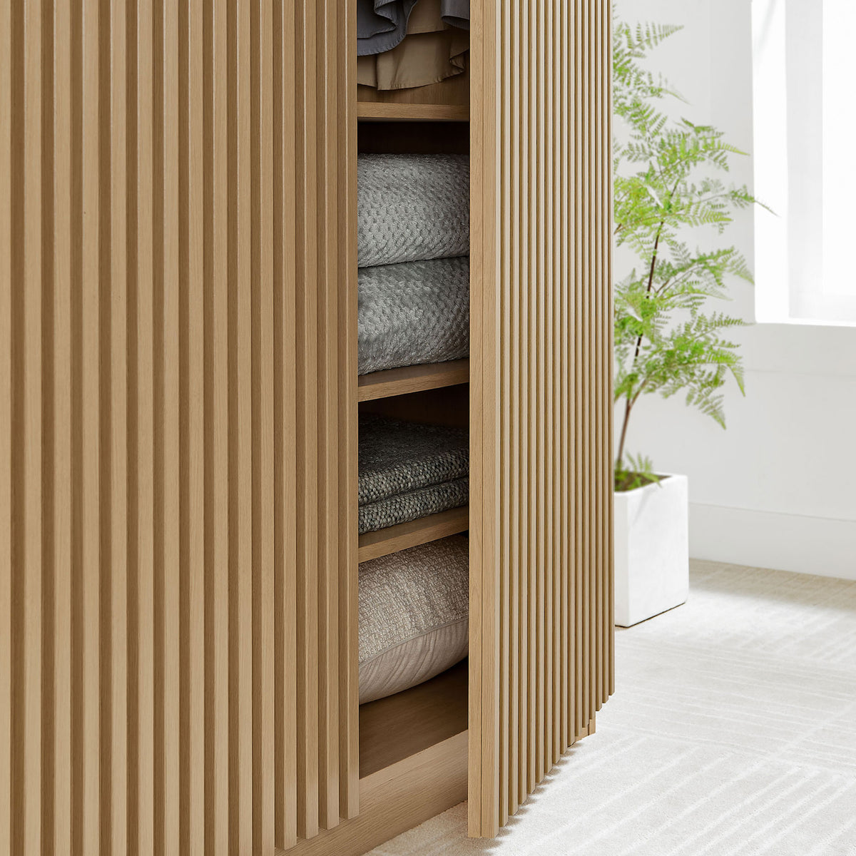 Oak wardrobe base with slatted door partially open to display folded blankets and linens on shelves || MOD-7182-OAK || storage_open_room