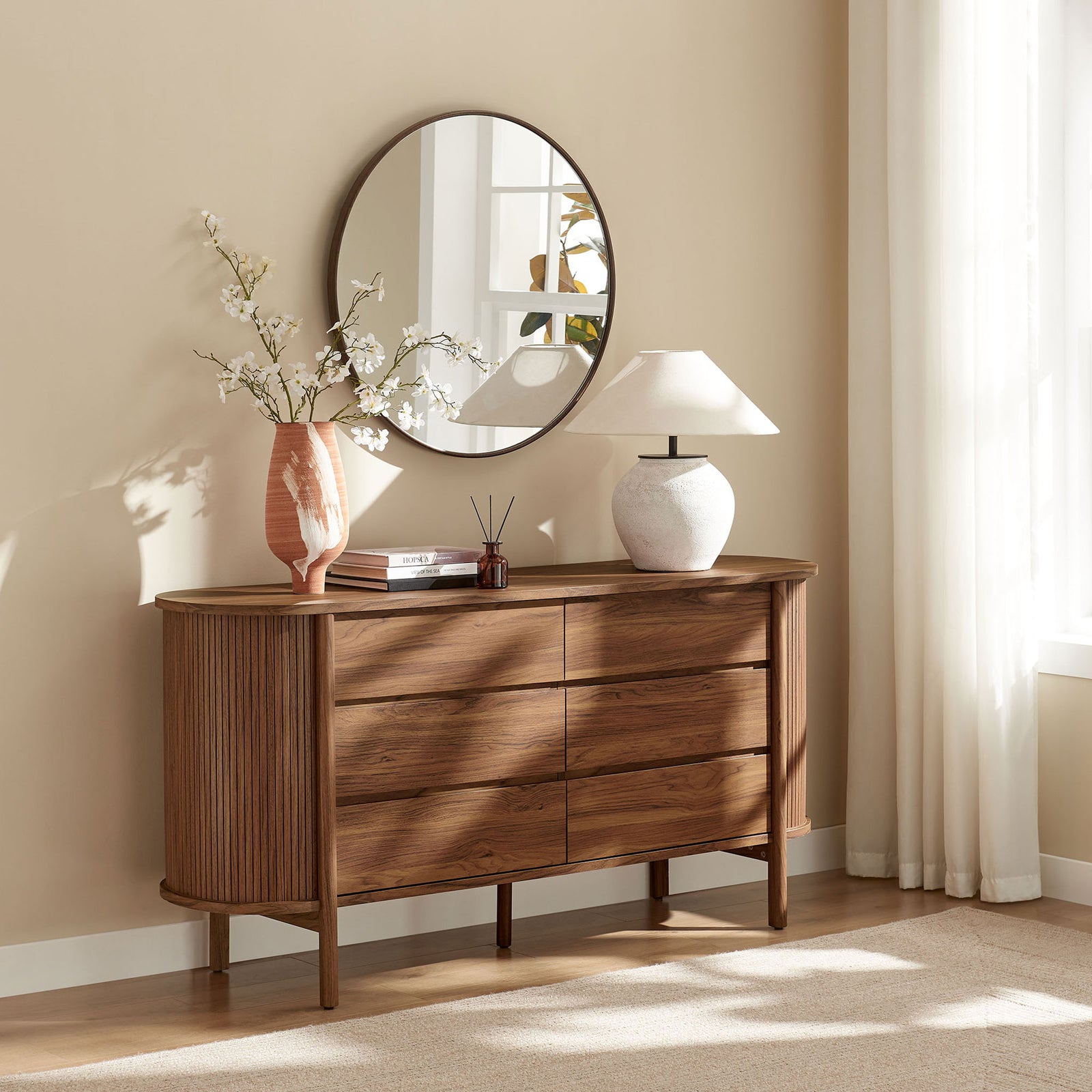 Curved walnut dresser in a bright bedroom setting, styled with a round mirror, vase, and table lamp || MOD-7242-WAL || front_room