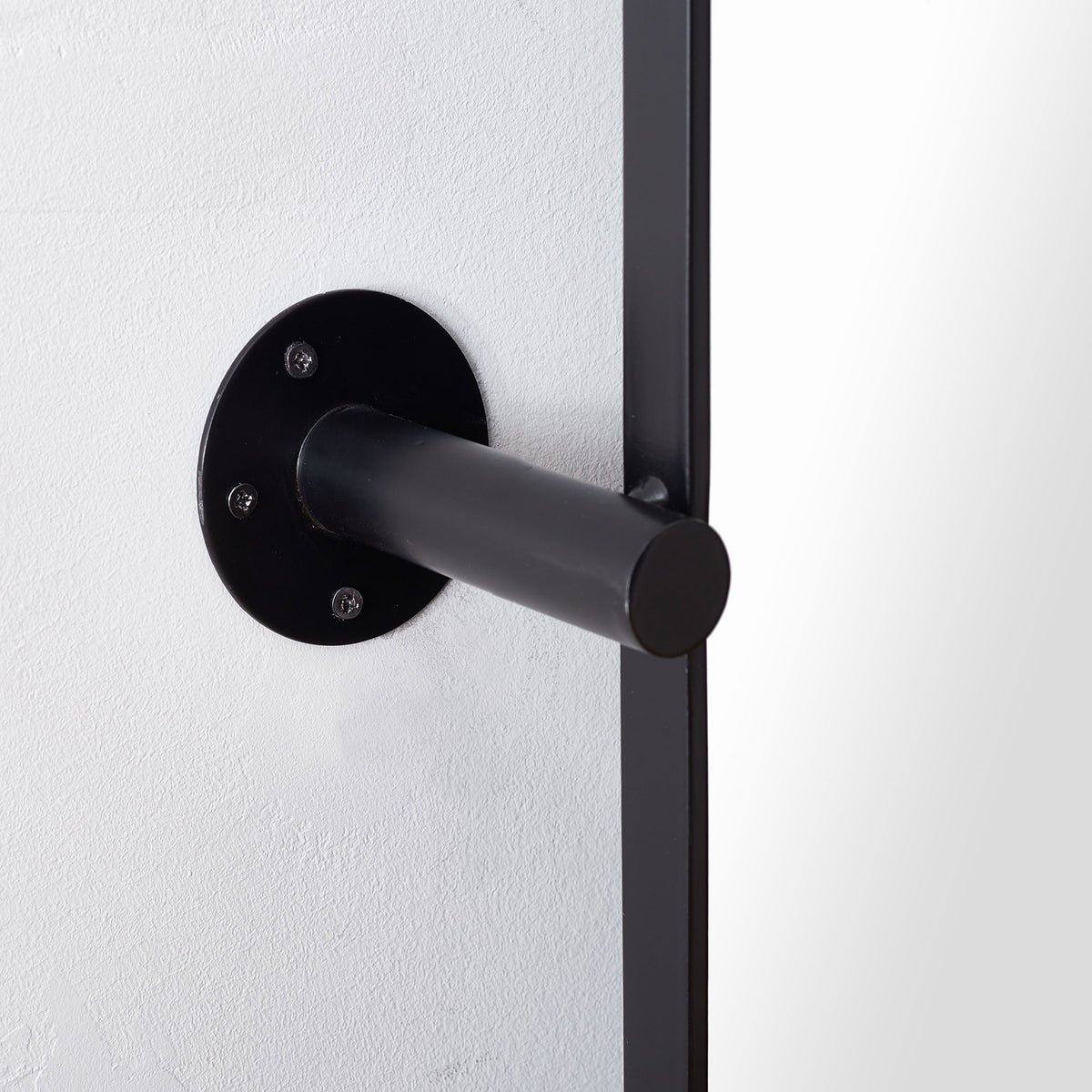 Black tubular support extends from a round, screw-mounted wall plate beside the mirror frame.