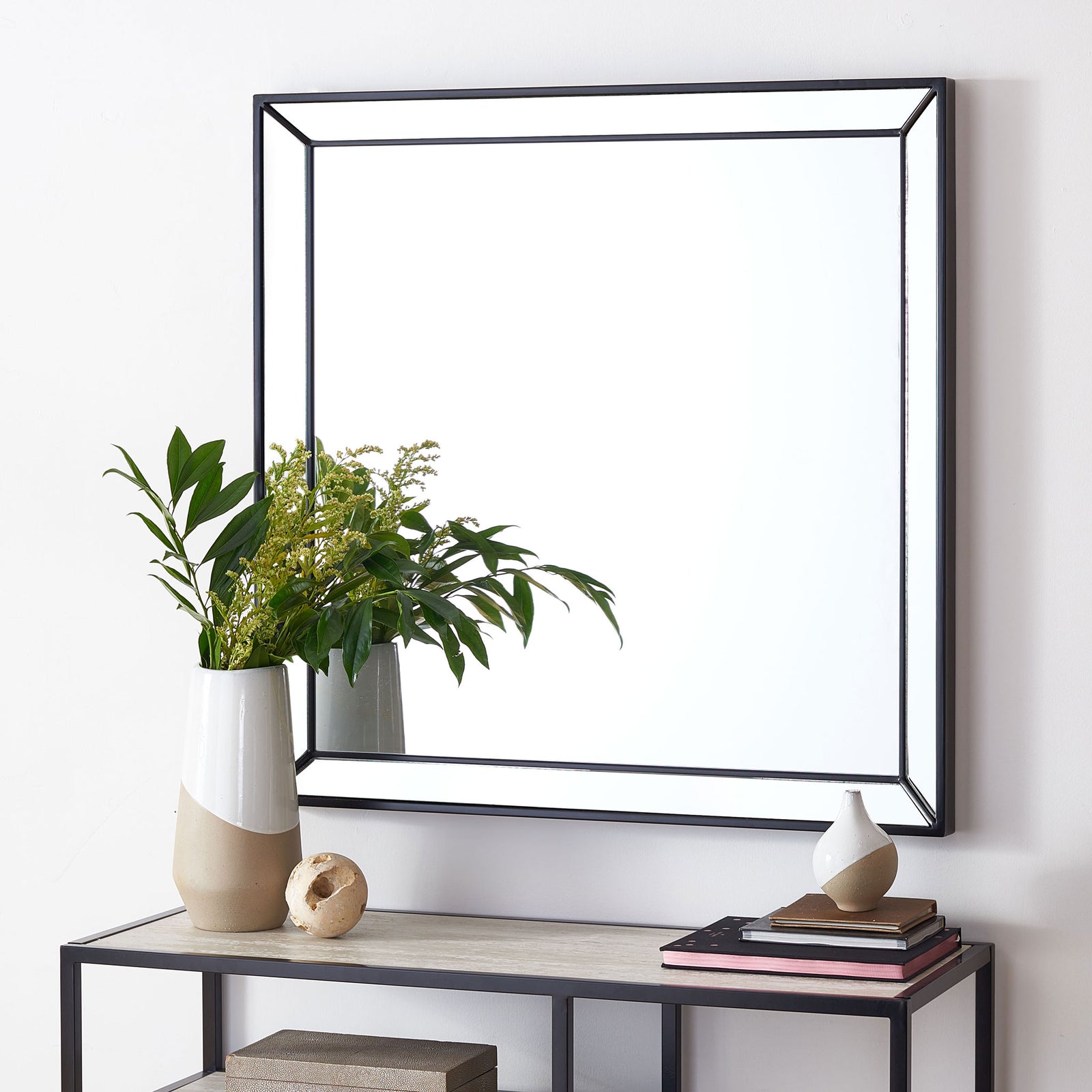 A sleek black square mirror adds clean geometry and reflected light above a console table. || MRR2004B || front_room