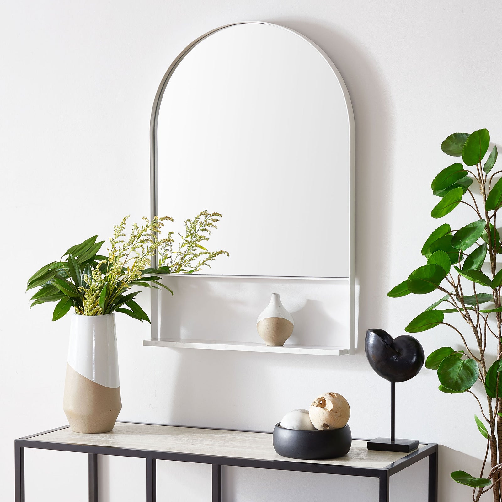 A white-framed arched mirror offers reflection and a slim shelf for decor above a console. || MRR2009B || front_room