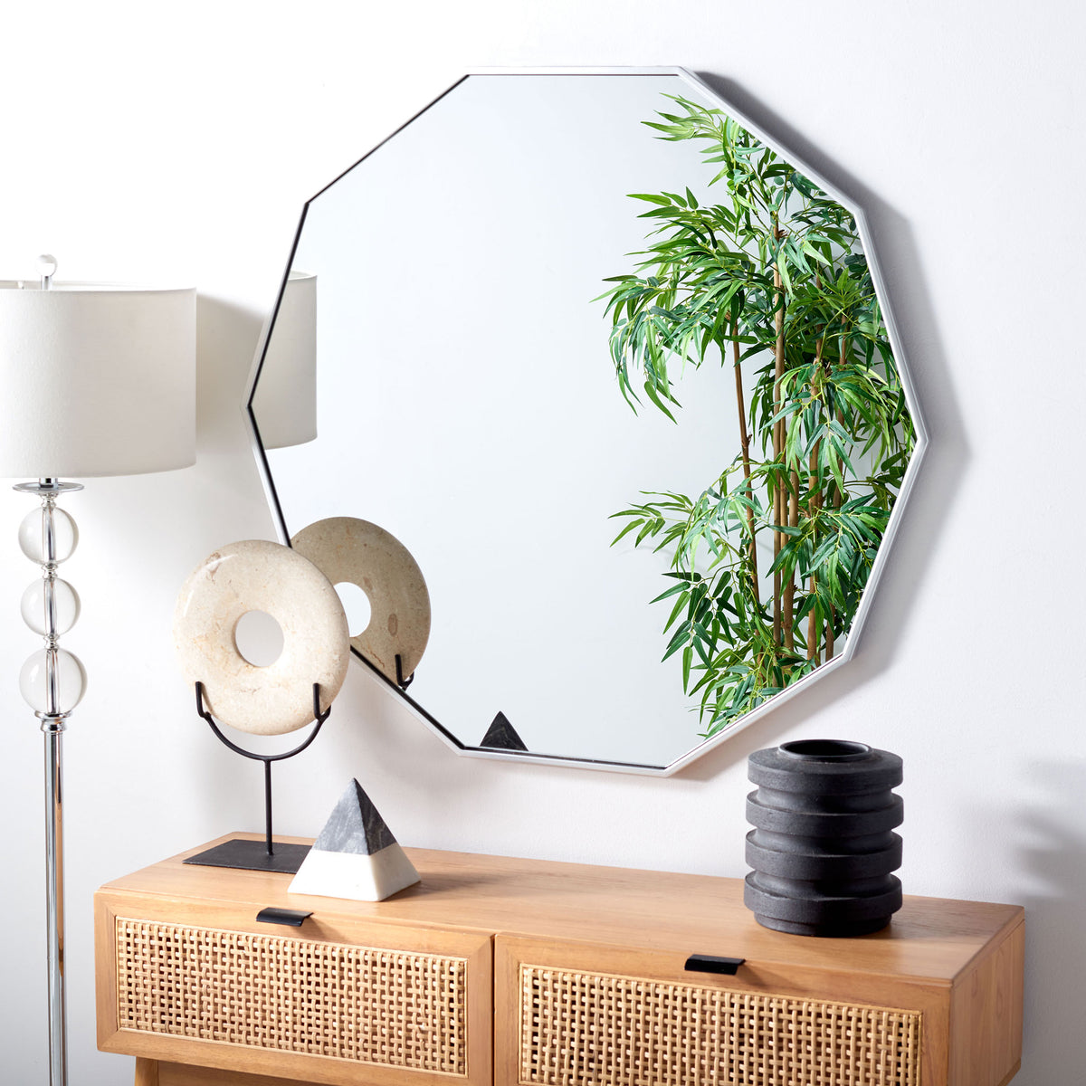 Silver-framed geometric mirror brightens the wall above a natural wood cabinet