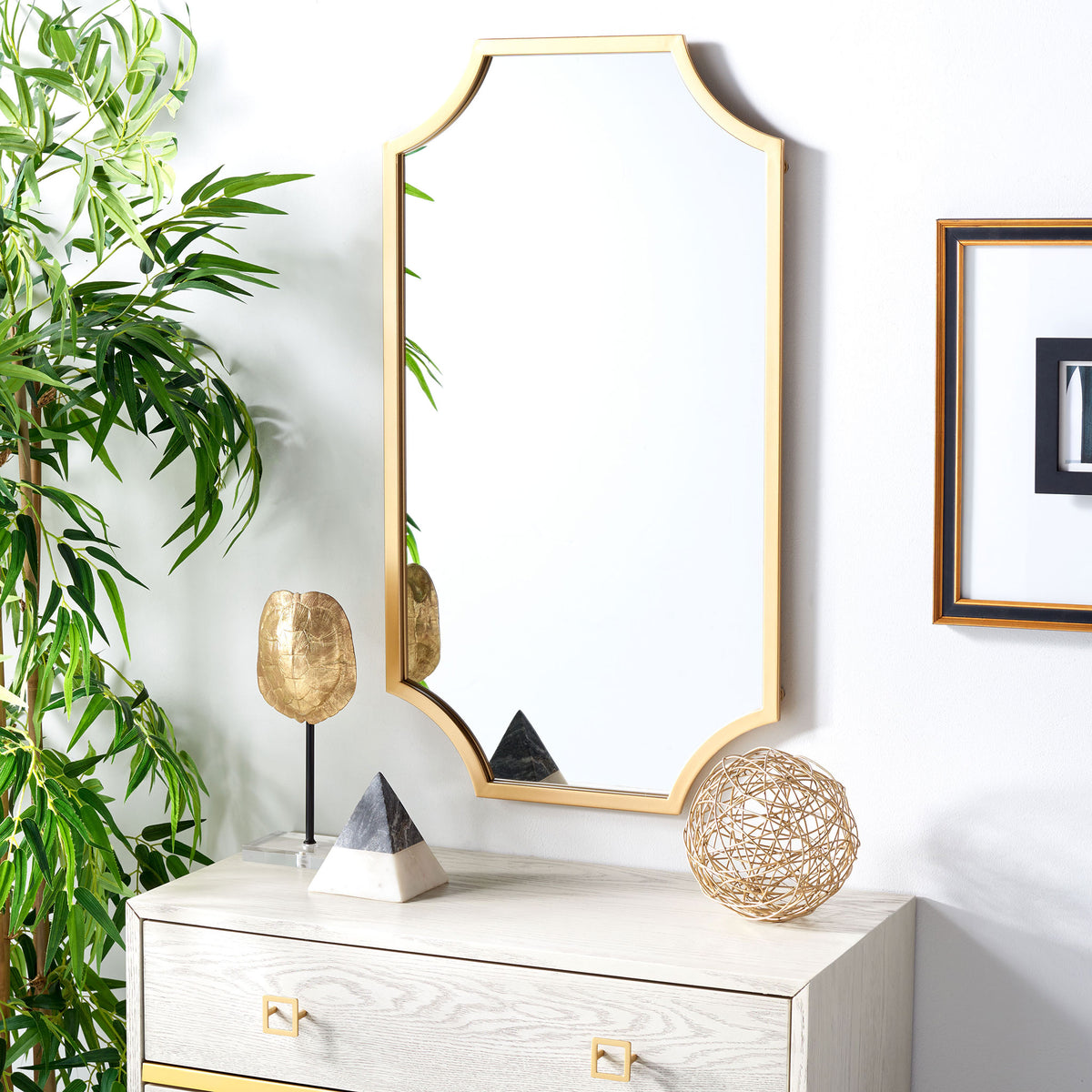 The brass-framed mirror brings a warm metallic accent to a bright wall above a dresser. || MRR2012A || front_room