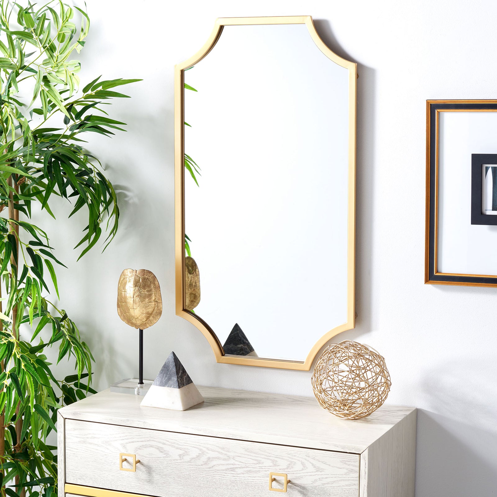 The brass-framed mirror brings a warm metallic accent to a bright wall above a dresser. || MRR2012A || front_room