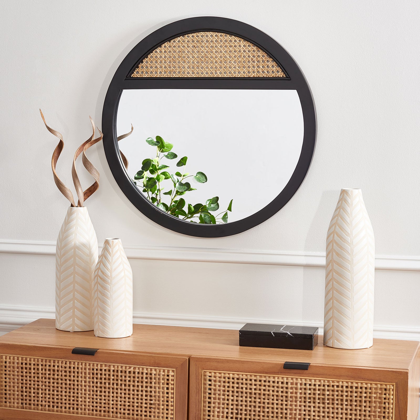 A round black mirror displays its woven cane accent at the top above a warm wood cabinet. || MRR2014A || front_room