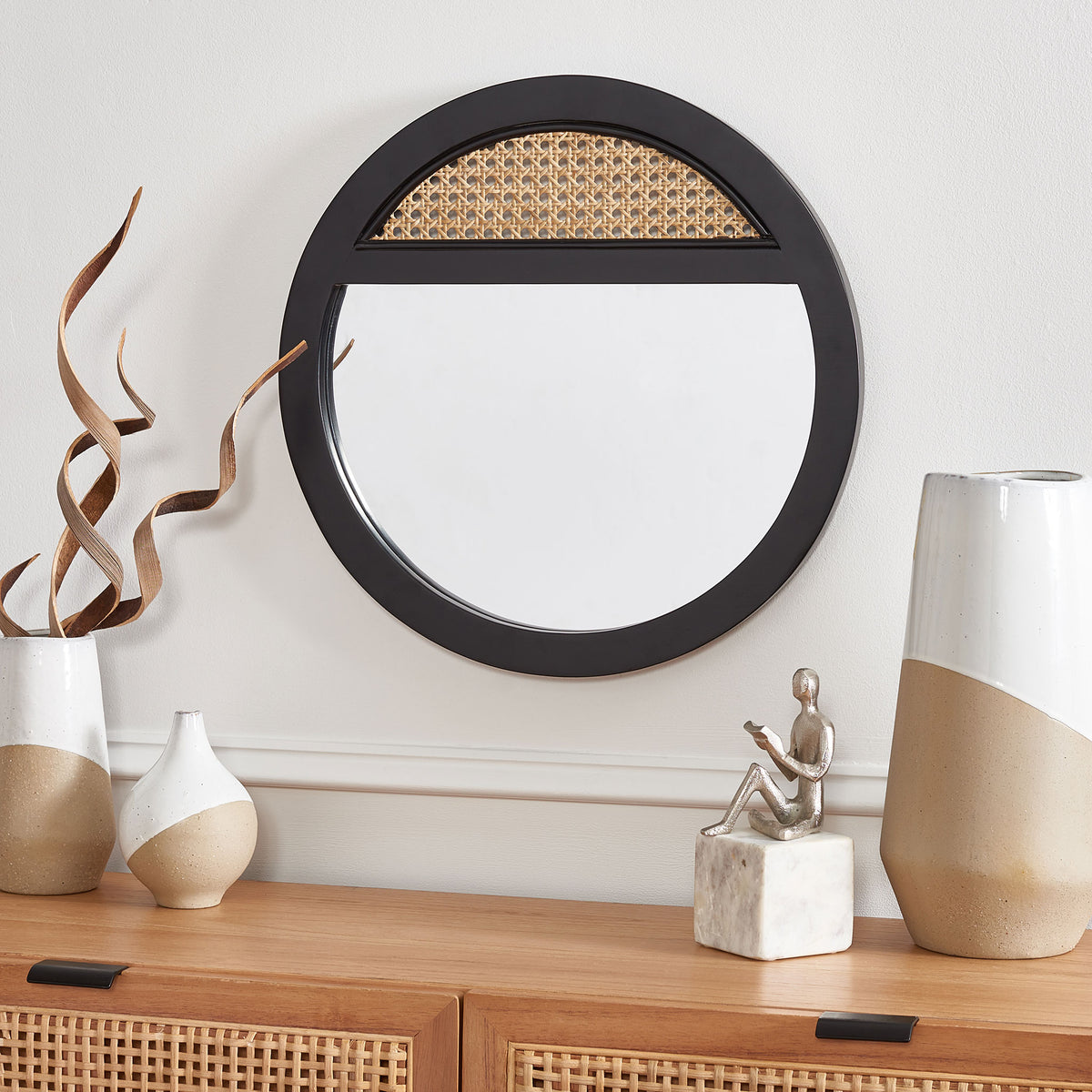 A black-framed mirror with a woven cane accent adds contrast above a wood console.
