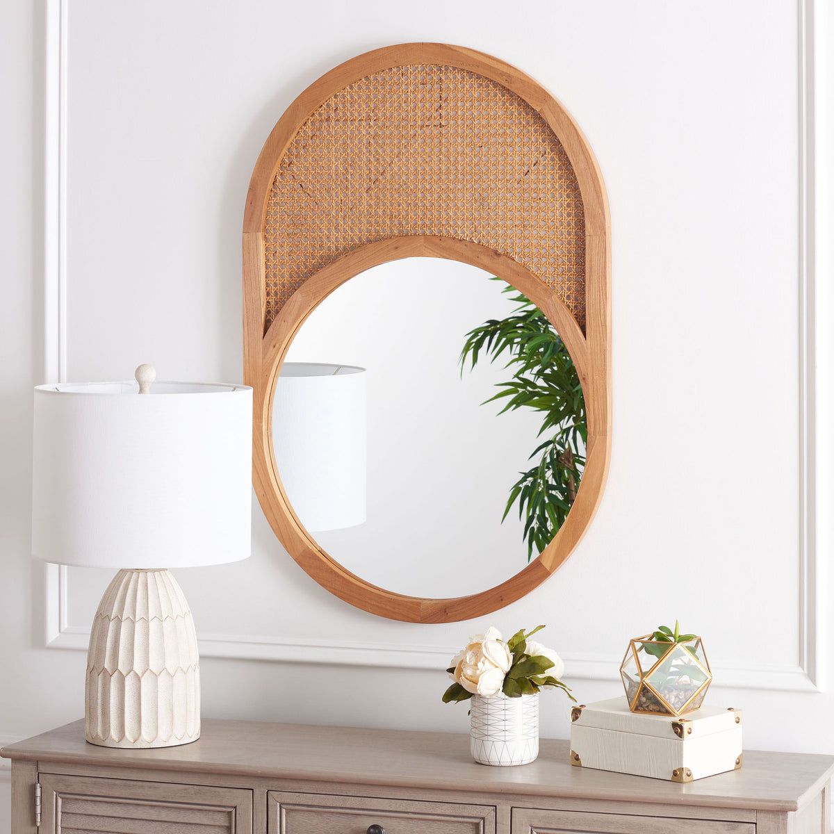 An oval natural wood mirror with woven cane above the glass lends warmth to a console display.