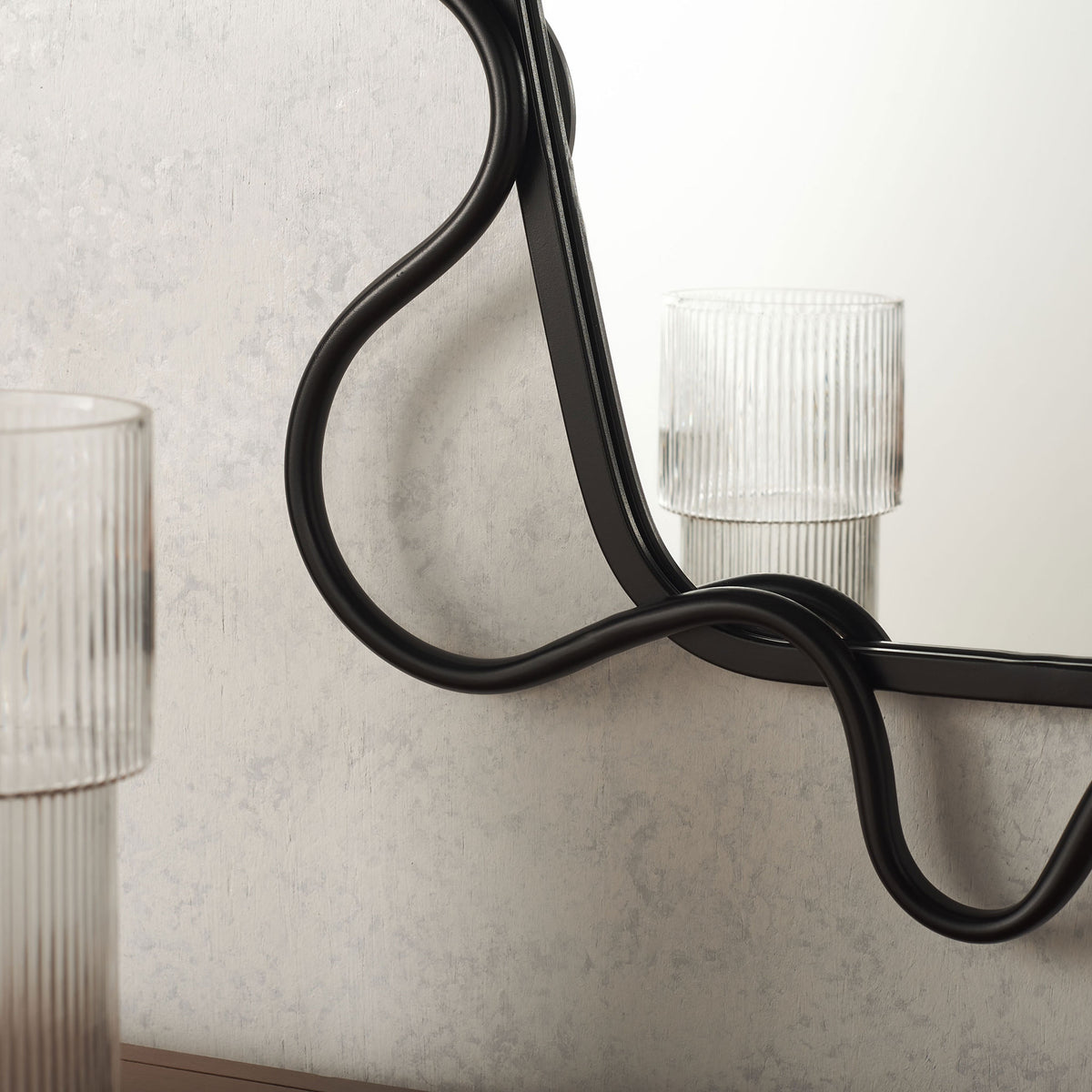 Black metal tubing curves around the mirror edge with an airy, flowing silhouette || MRR2500A || detail_room